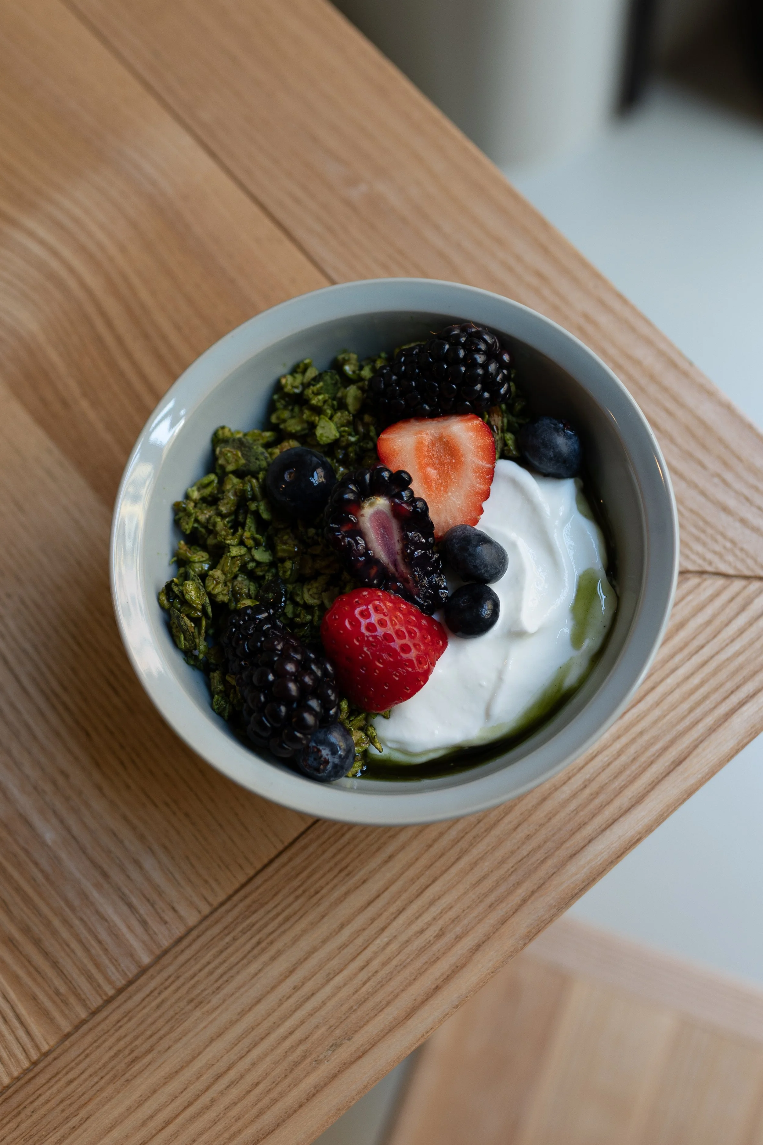 Ciotola di yogurt con frutti di bosco, fragole, mirtilli, lamponi, semi di chia, e granola, su un tavolo di legno.