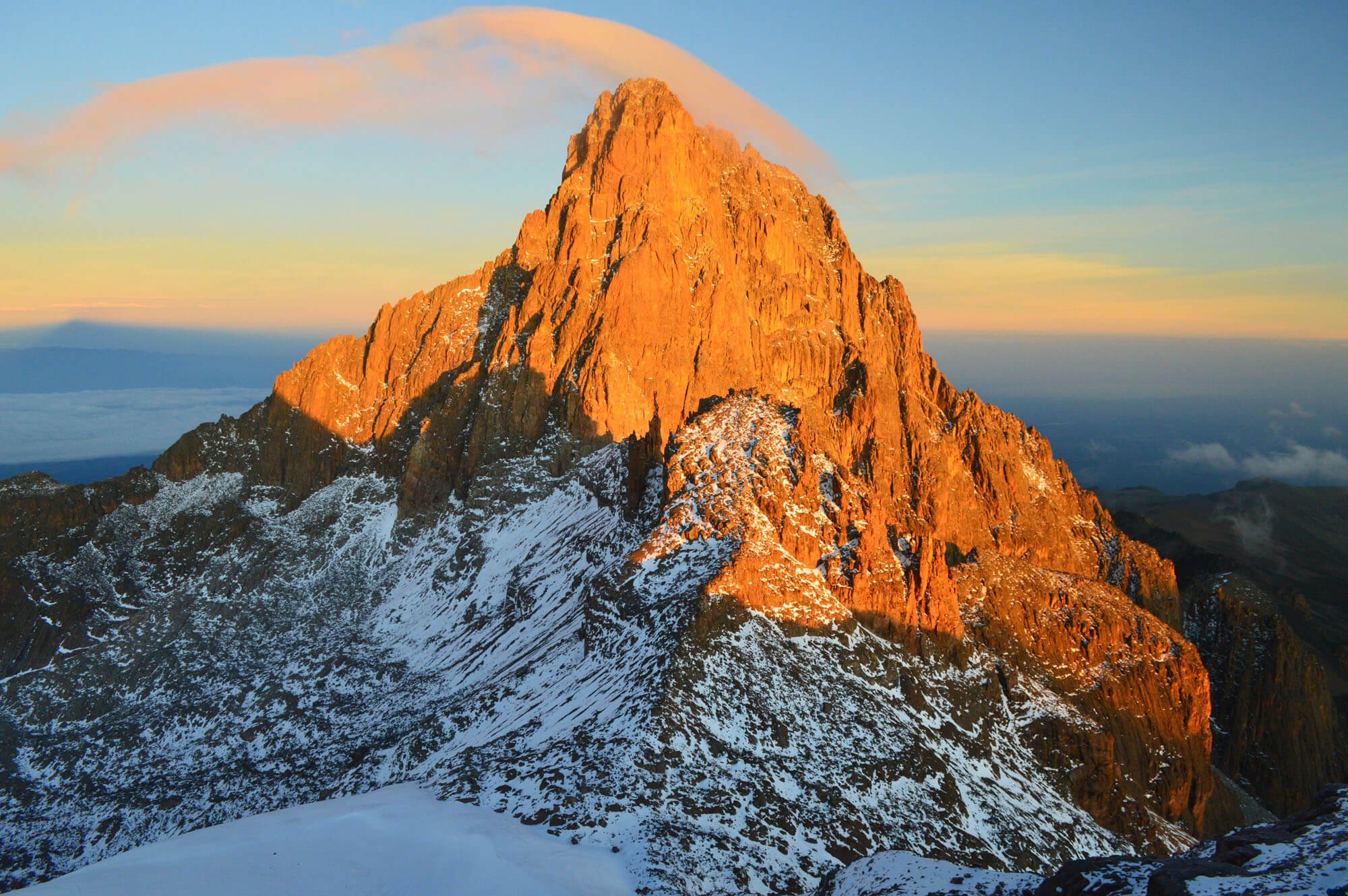 Sunlit mountain peak with snow-capped slopes during sunset or sunrise with a partly cloudy sky.