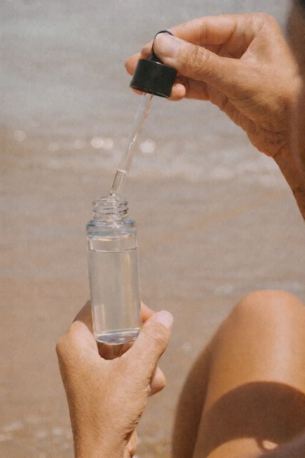 Woman's hands holding a glass dropper bottle at the beach