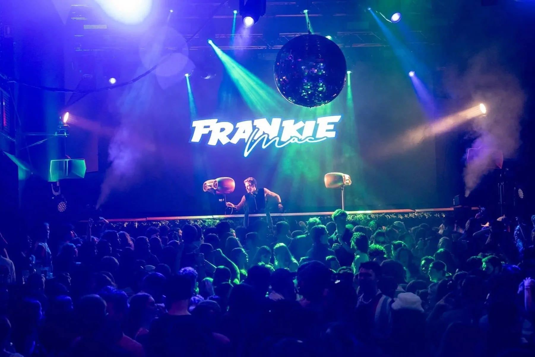 A live electronic dance music concert with a DJ on stage, colorful lighting, a large screen displaying 'Frankie Ma' logo, and a crowd of fans dancing.