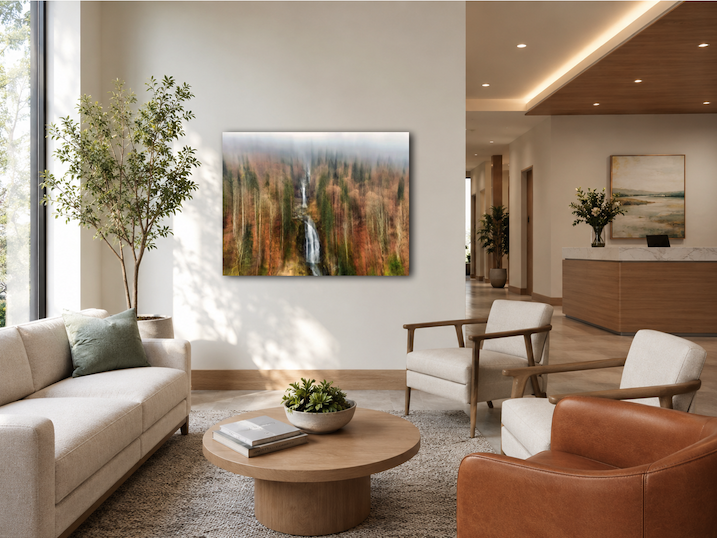 Moderne, helle Hotellobby mit weißem Sofa, zwei weißen Sesseln, einem braunen Sessel, einem runden Couchtisch mit Büchern und einer Schale mit Pflanzen, großen Fenstern und Wandkunst, Stehlampen, Pflanzen, und einem Empfangstresen im Hintergrund.