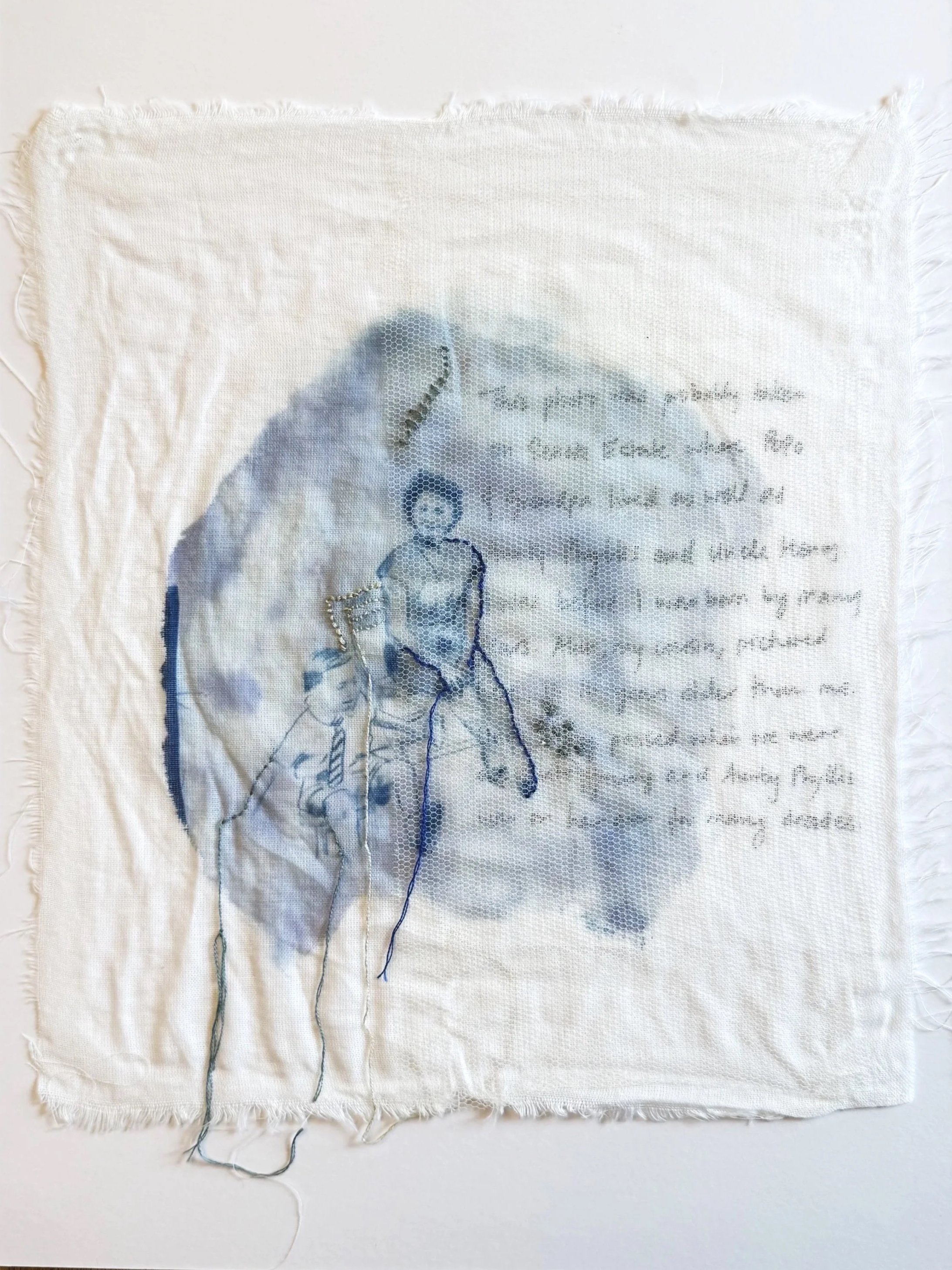 A fabric piece with a cyanotype printed and embroidered design featuring a seated woman and a small child  with handwritten text in the background.