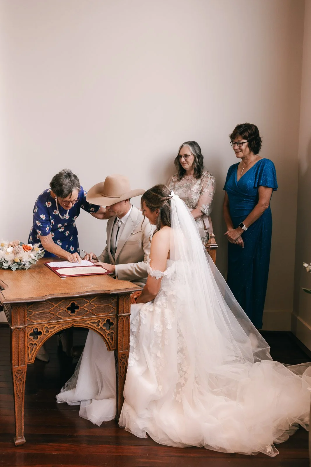 A bride and groom signing a marriage license with family members observing in a room.