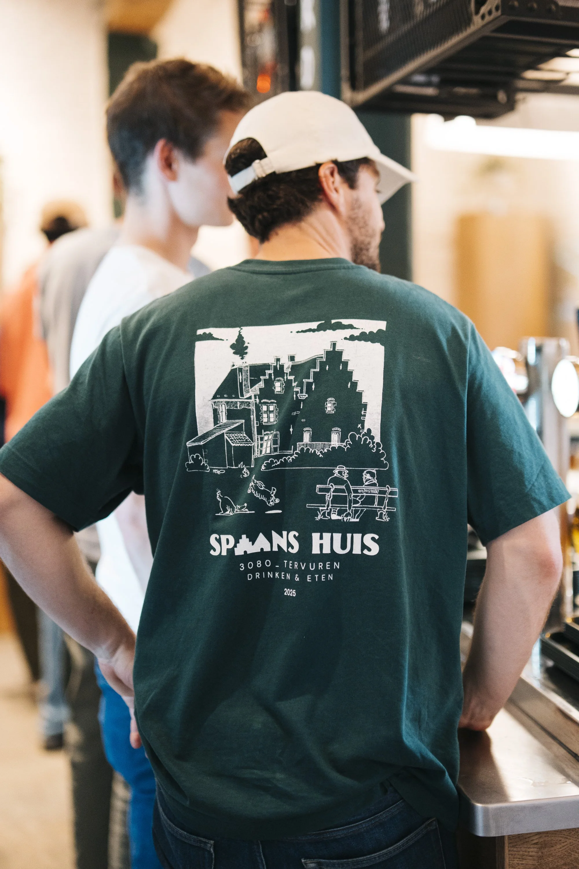 A man in a green T-shirt with a white graphic of the Spaans Huis!