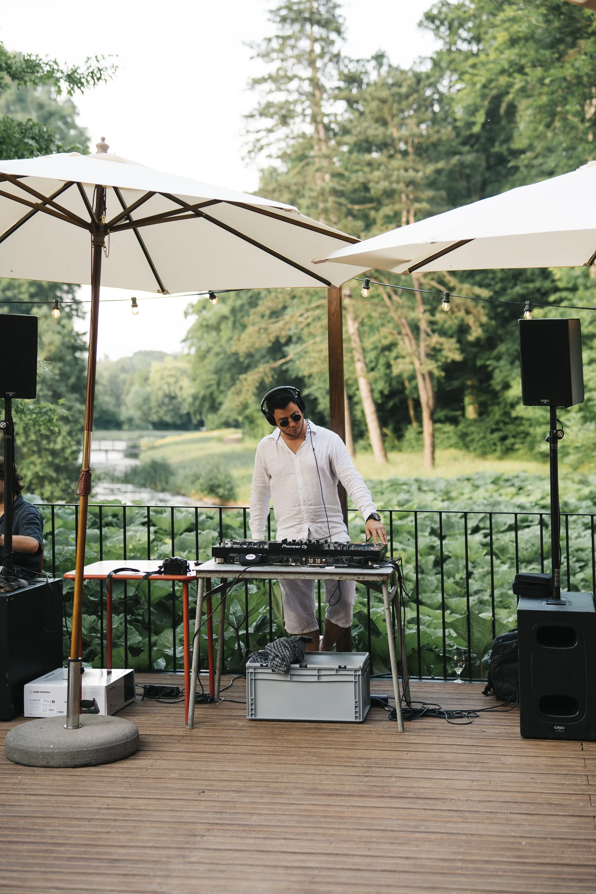 DJ performing outdoors on a wooden deck with large umbrellas and a scenic green background. At Spaans Huis Tervuren.