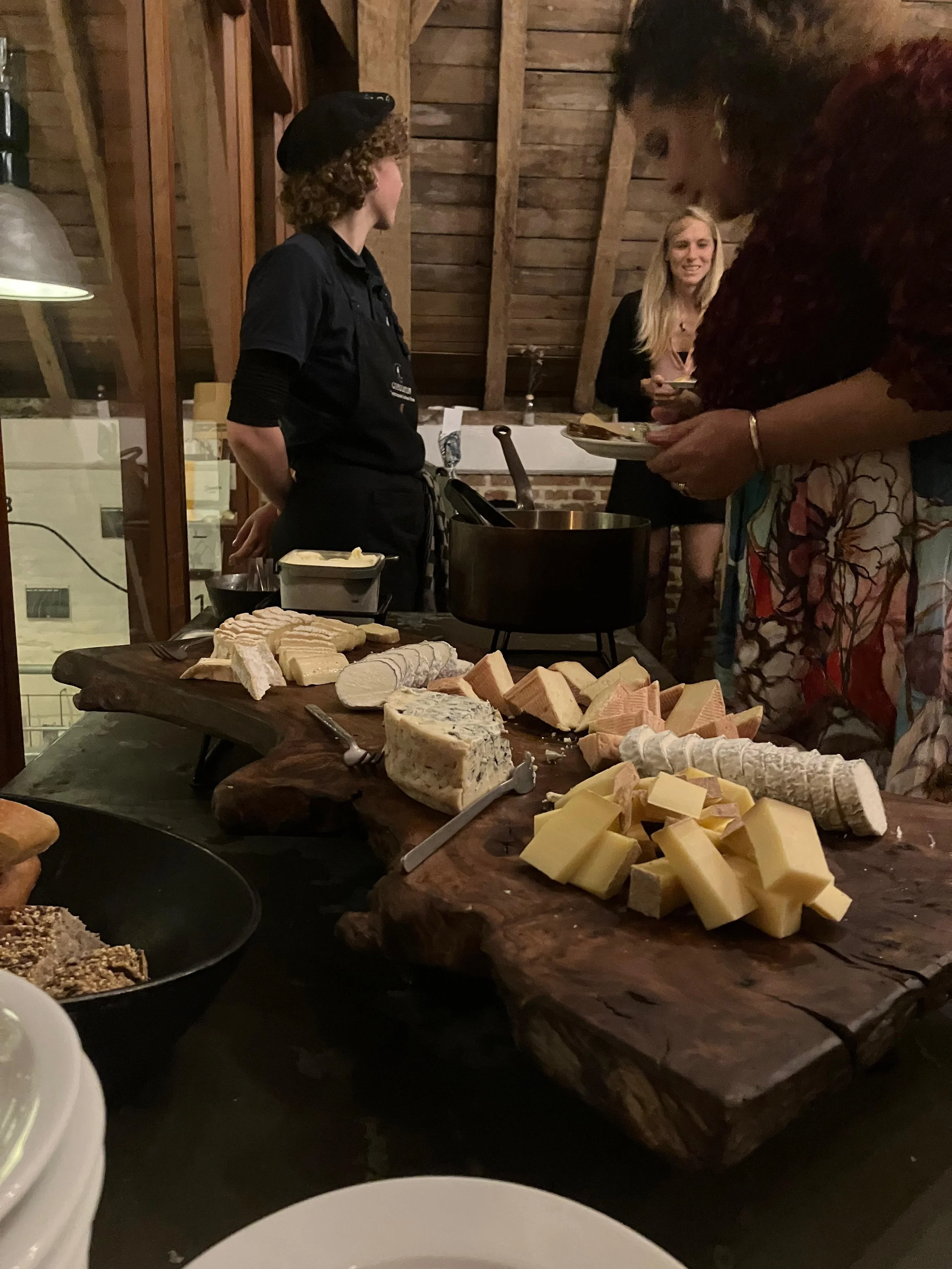 Cheese display on a rustic wooden board at a cheese tasting event, with guests in the background. At Spaans Huis Tervuren.