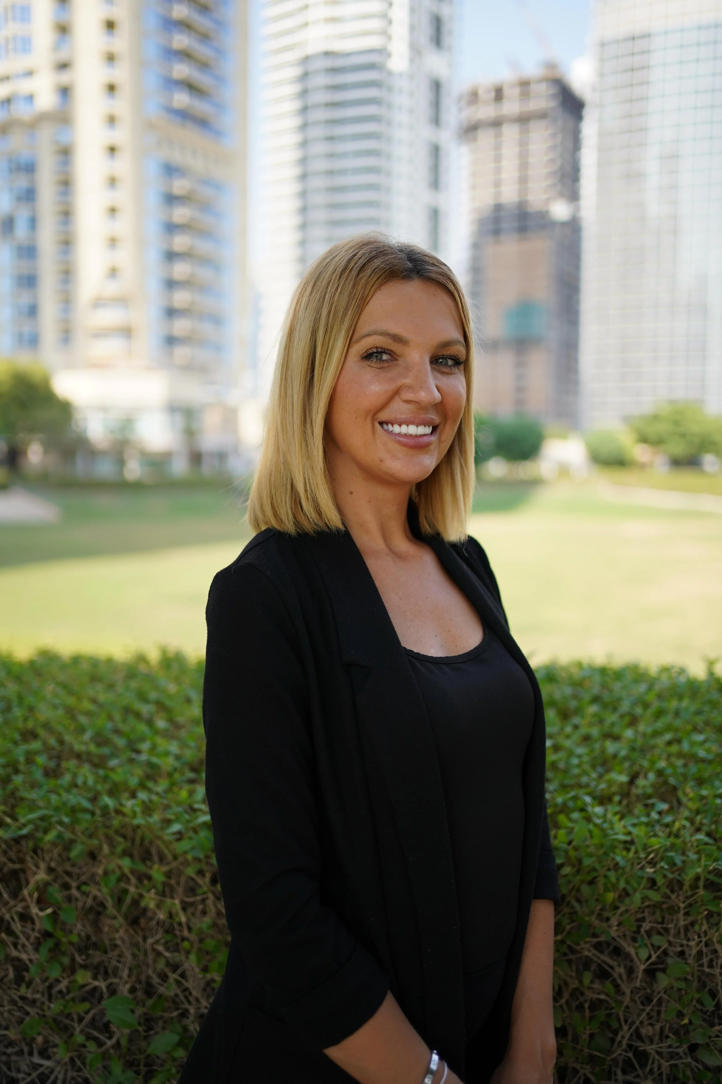 A smiling woman with long brown hair wearing a black blazer, posing against a gray background.