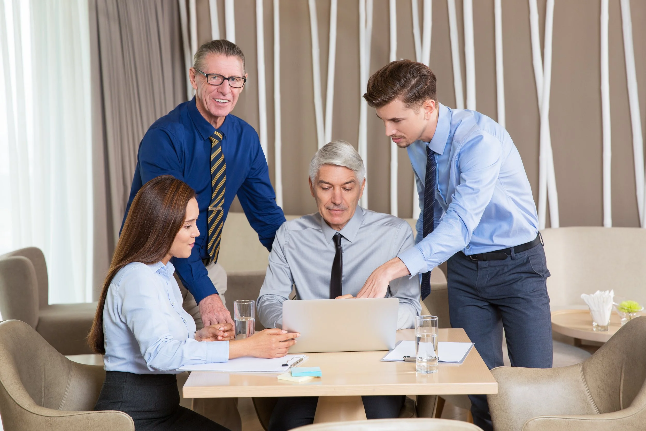 Group of five diverse business professionals gathered around a laptop during a meeting, discussing work in a conference room.