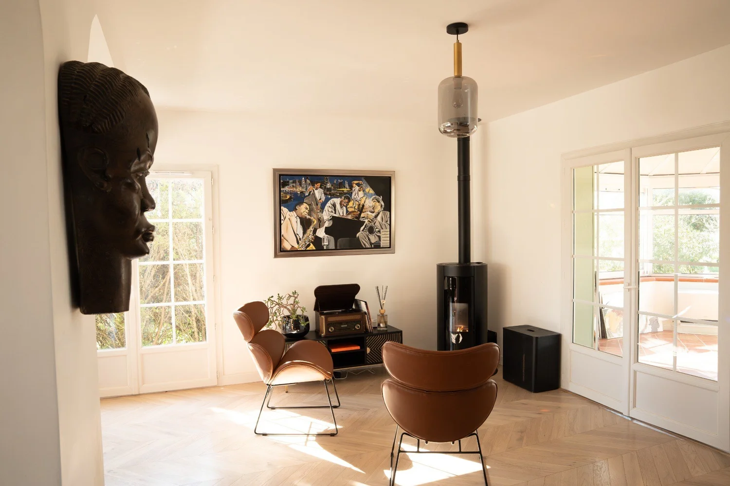 Salon Aussonne, fauteuils en cuir et poêle noir dans une pièce ouverte sur le jardin
