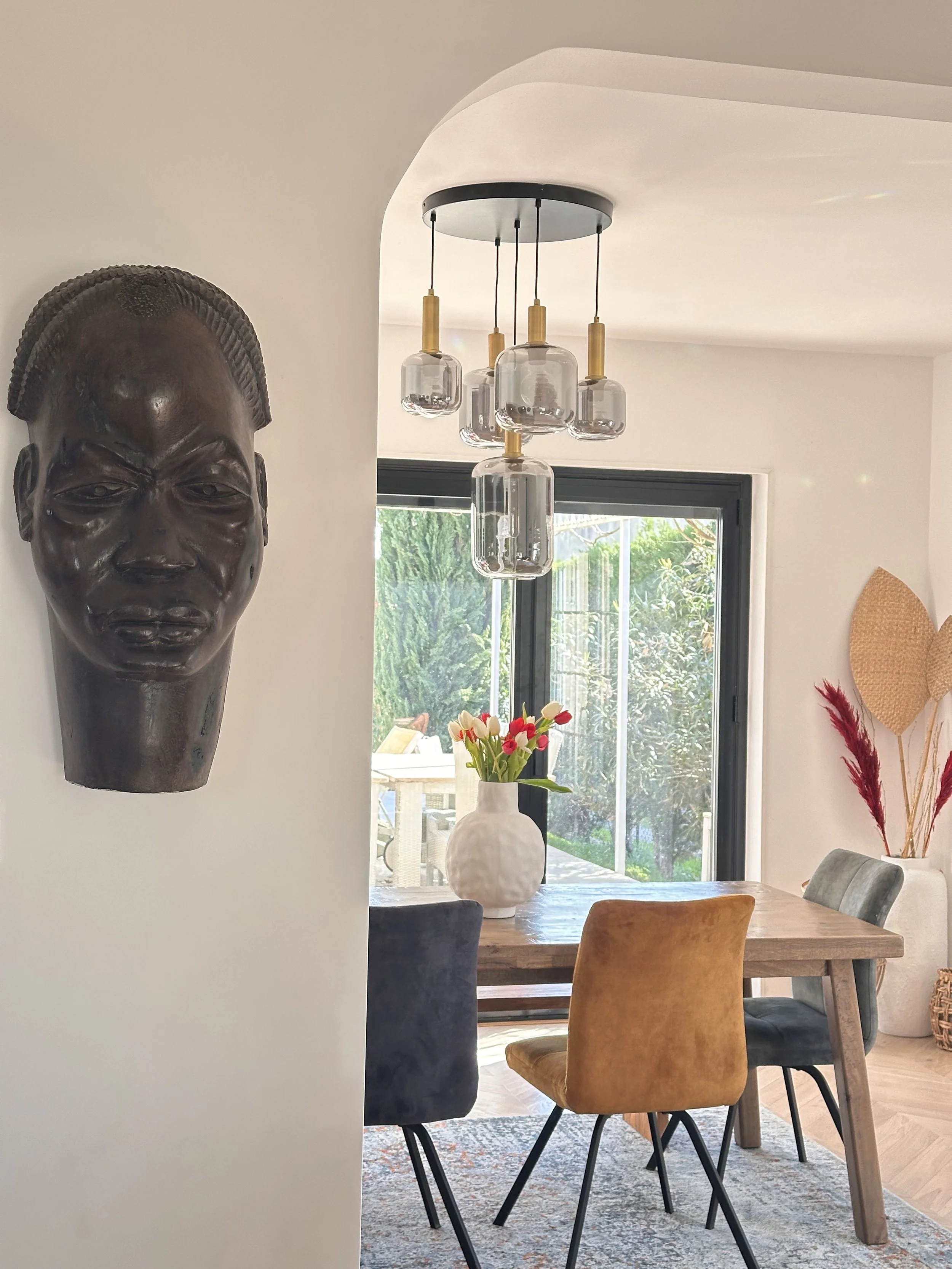 Salon en rénovation avec sol en bois clair, fenêtres grandes avec vue sur jardin, et meubles en plastique et cartons sur le sol.