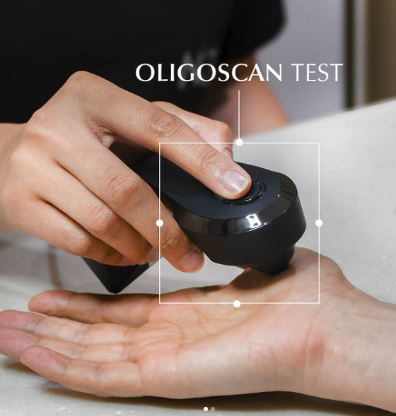 A hand holding an Oligoscan device testing a person's palm on a table.