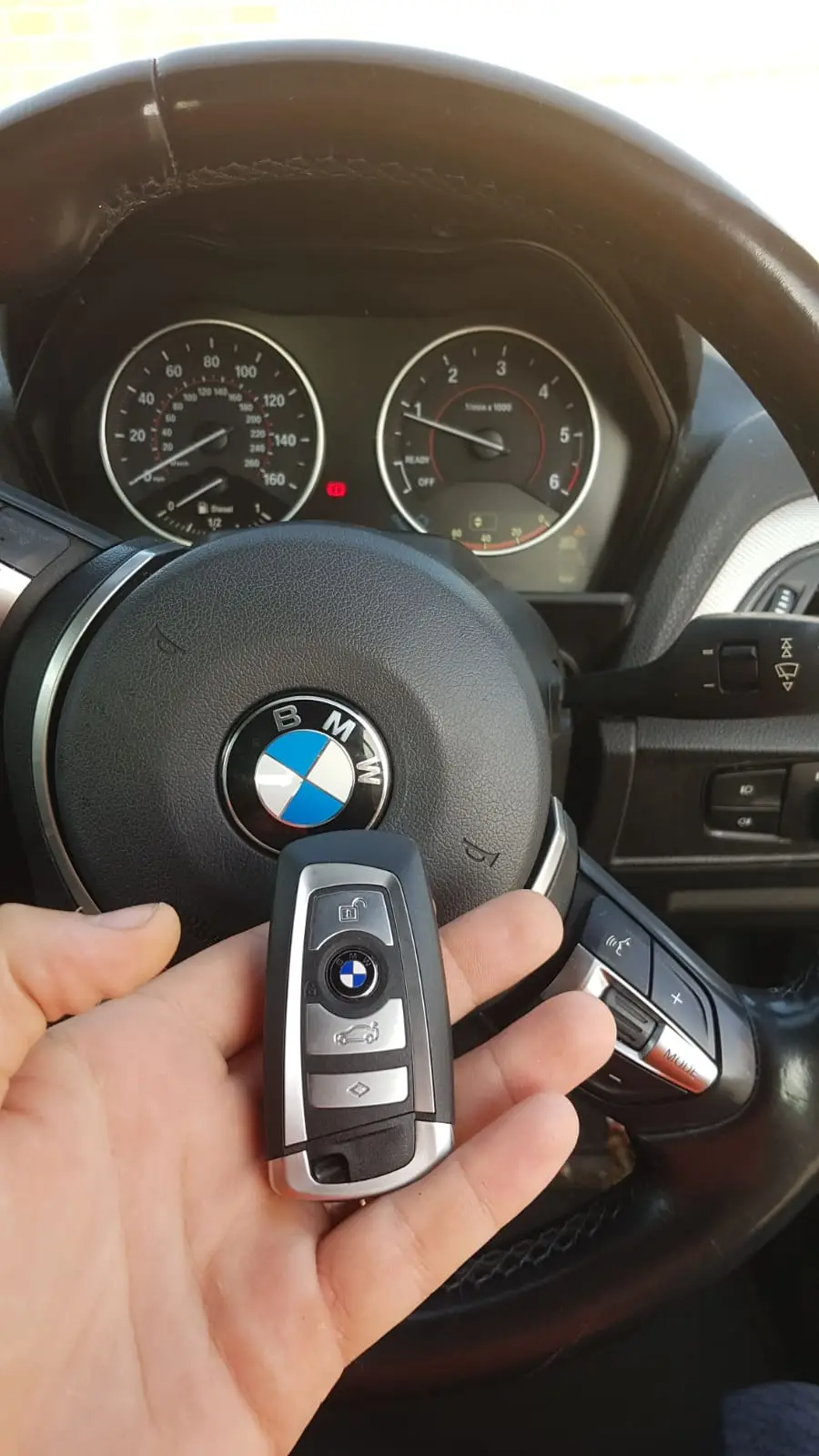 Bilnøgle foran rat i en BMW, bilens instrumentbræt i baggrunden.