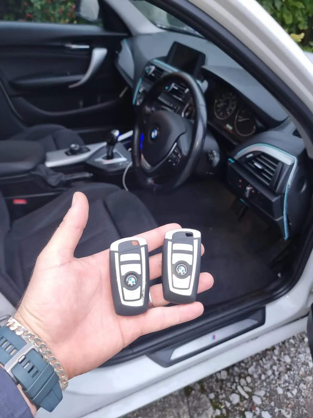 En person holder to BMW nøgler foran en bils indre, med førersædet og rat synligt.