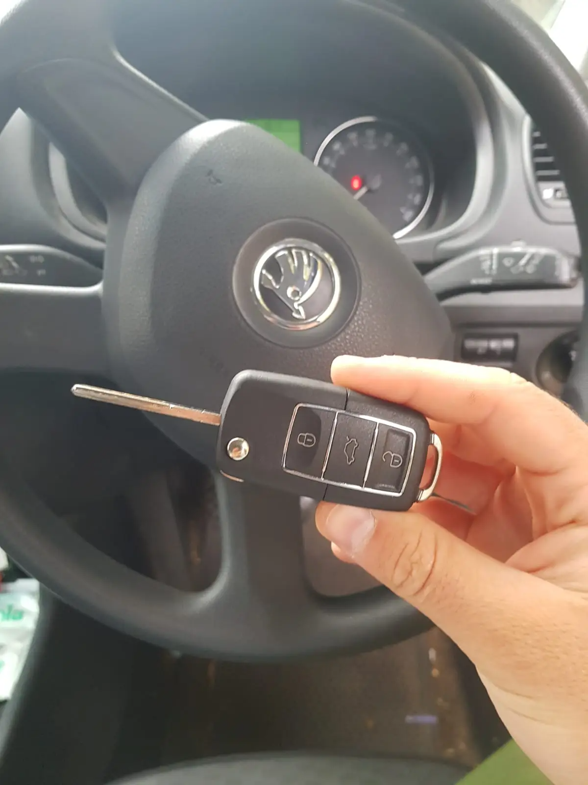 Person holder bilnøgle foran bilrat, hvor der er et Volkswagen logo. Indeni bilen ses rat, instrumentbræt og del af en kontroller.