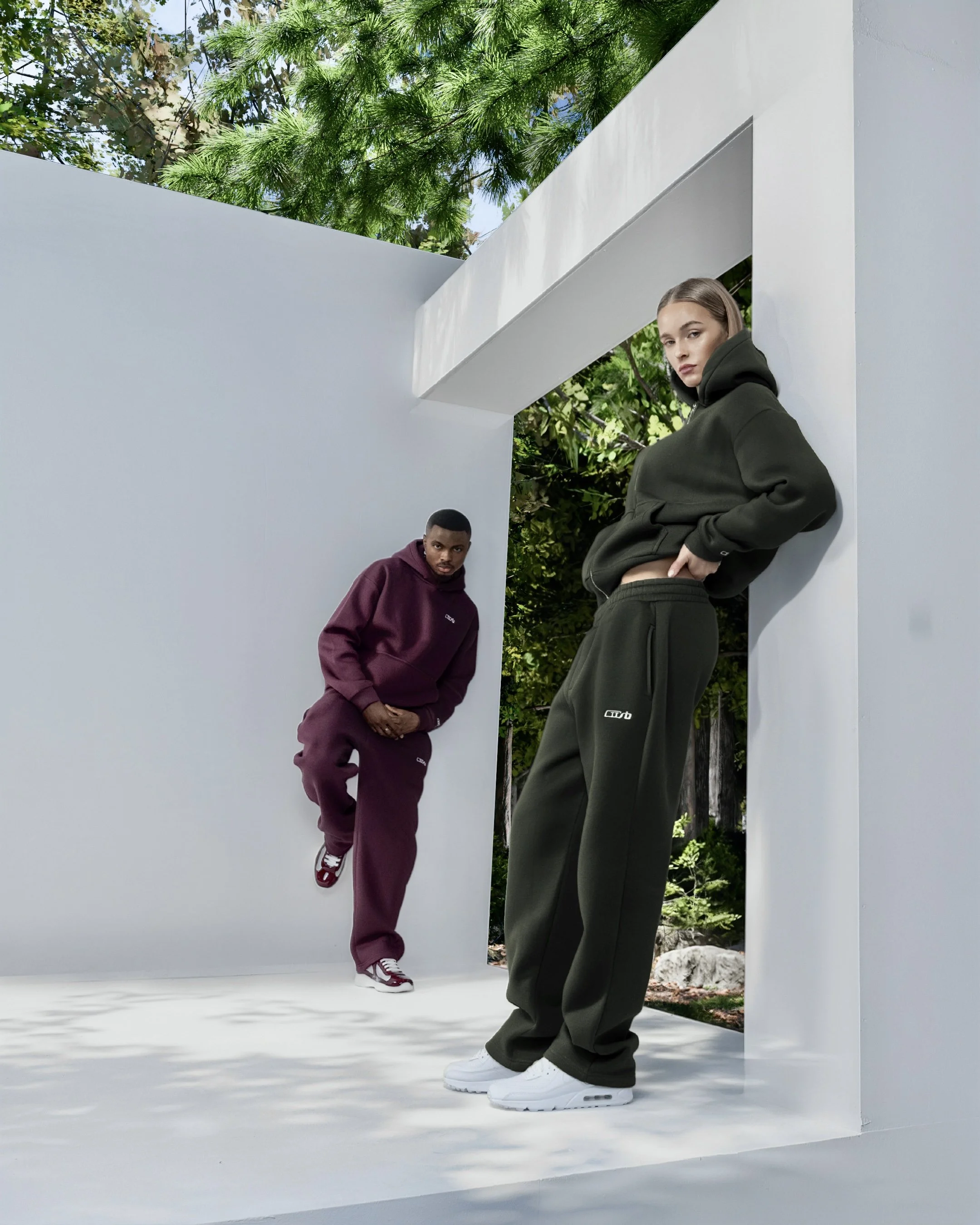 Zwei Modelle tragen CUSB Hoodies und CUSB Jogginghosen in einer minimalistischen, modernen Architektur mit weißem Hintergrund.