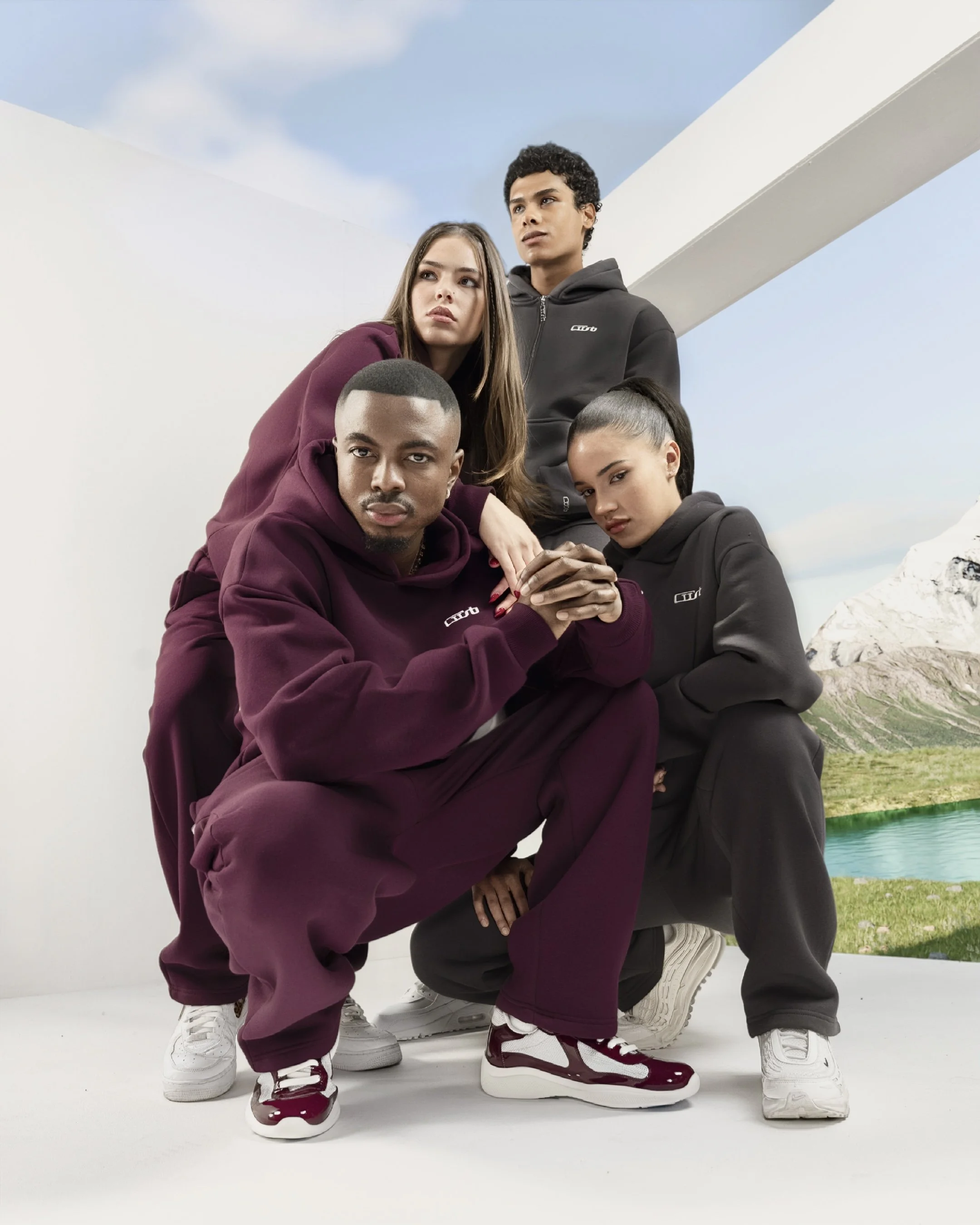 Vier junge Erwachsene in CUSB-Streetwear posieren vor einer Kulisse mit Bergen, See und Himmel, einige sitzen, andere stehen, tragen Hoodies und Sneakers.