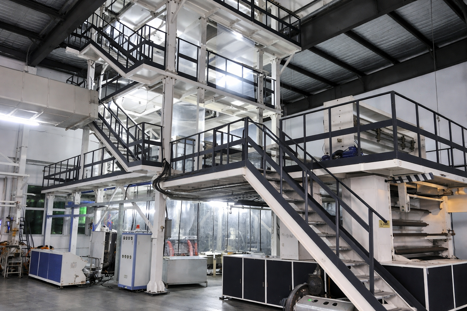 Industrial factory interior with metal stairs, walkways, and machinery in a clean, well-lit environment.