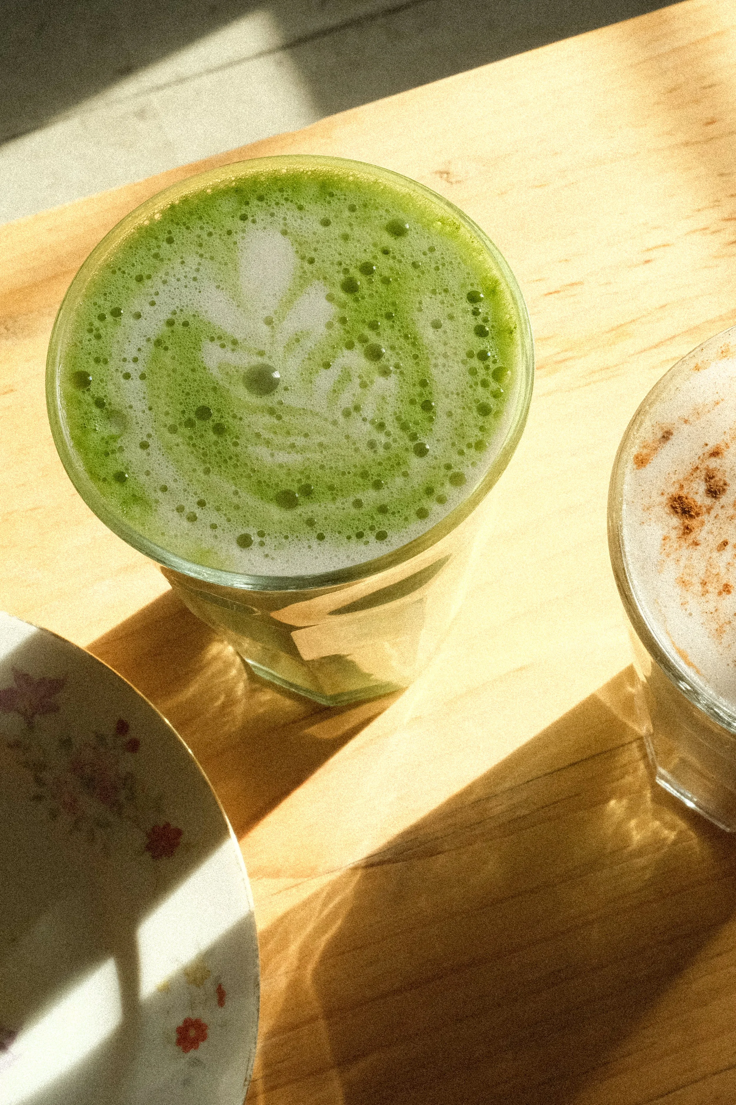 A glass of green matcha latte with latte art, sitting on a light wooden surface.