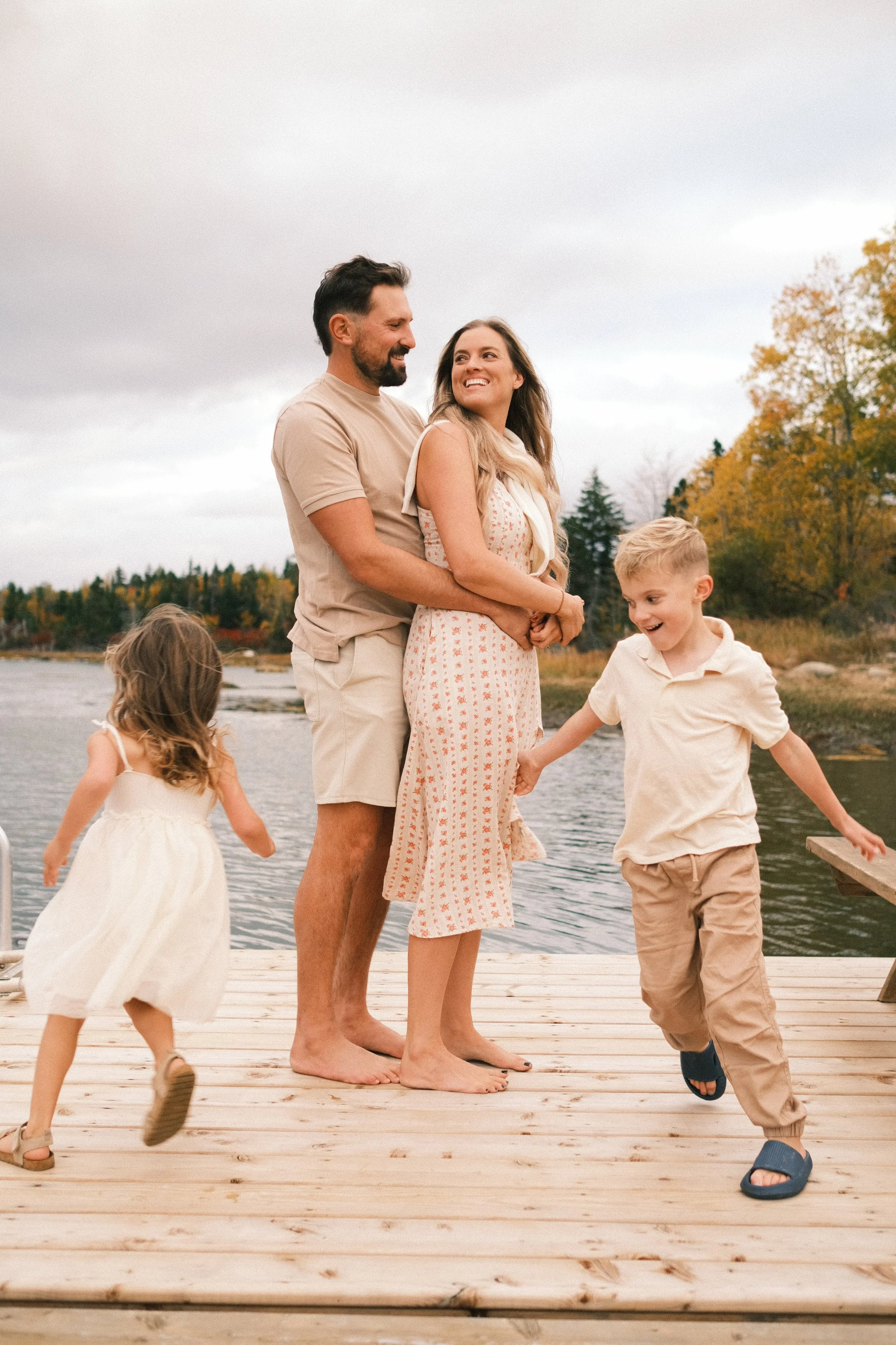 A family of four with two children enjoying time on a wooden dock by a river during fall, with autumn trees in the background.