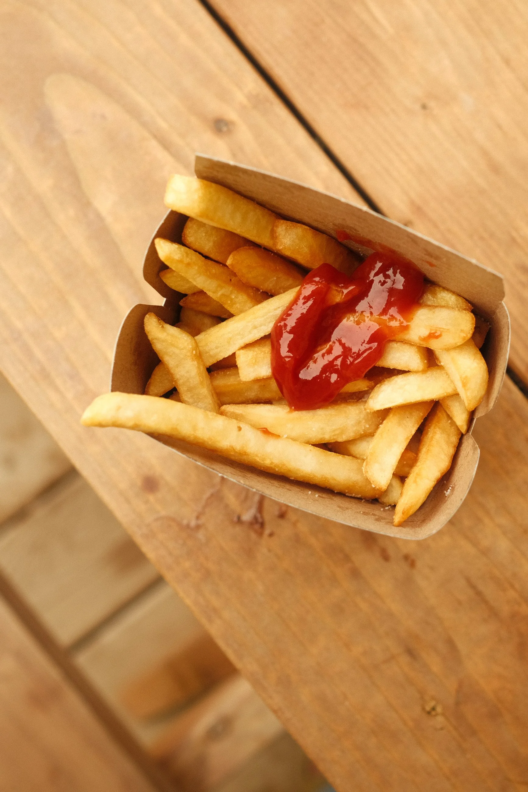 French fries with ketchup in a paper boat on a wooden table.