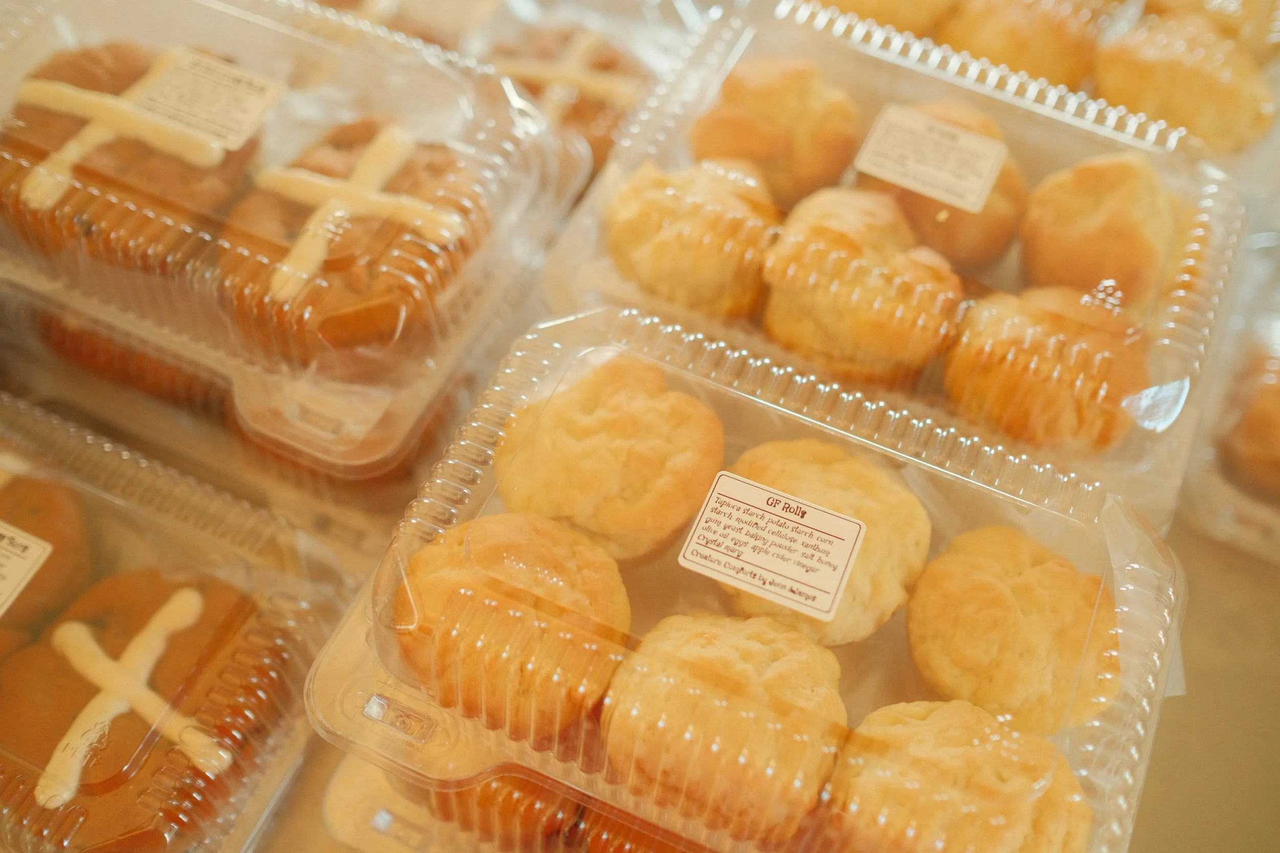 Packaged baked goods, including bread rolls and pastries, in clear plastic containers with labels.