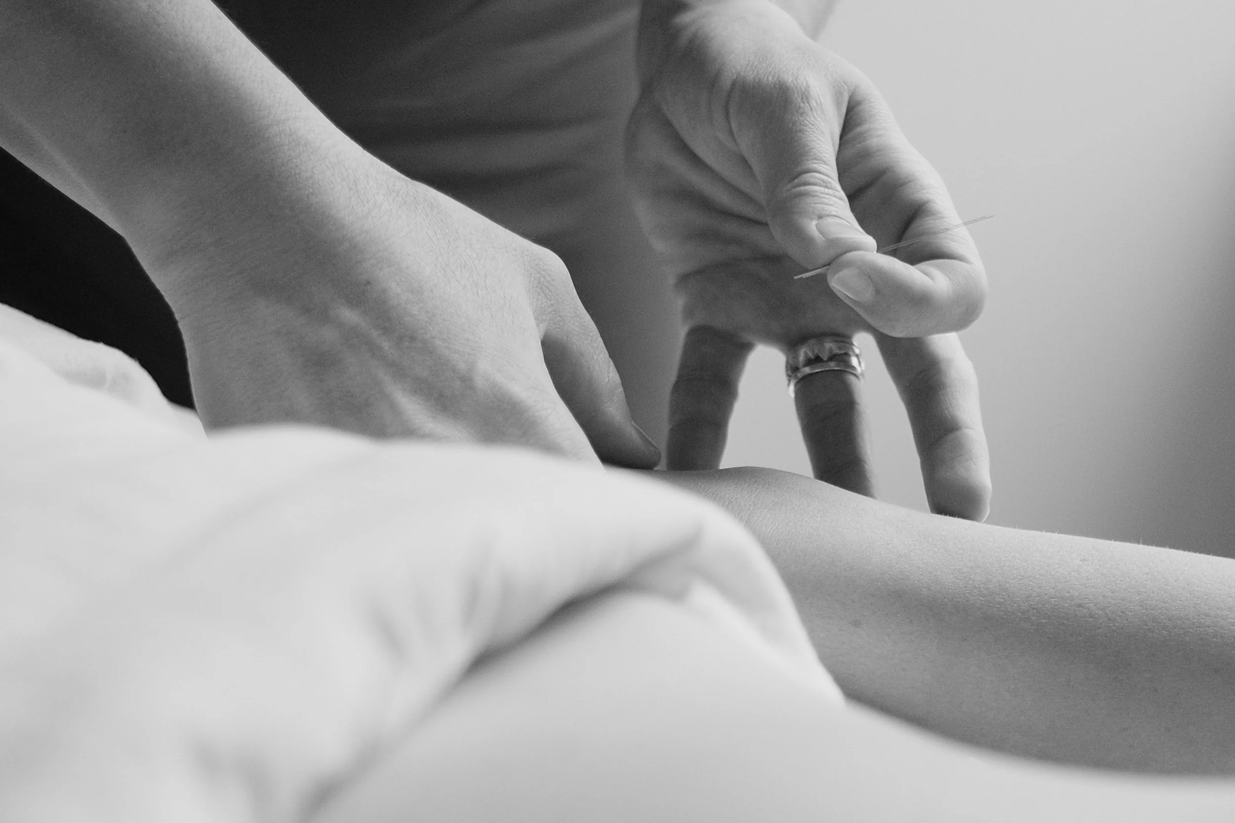 Close-up of someone giving a massage or physical therapy to a person's leg, focusing on the hands and leg in black and white.