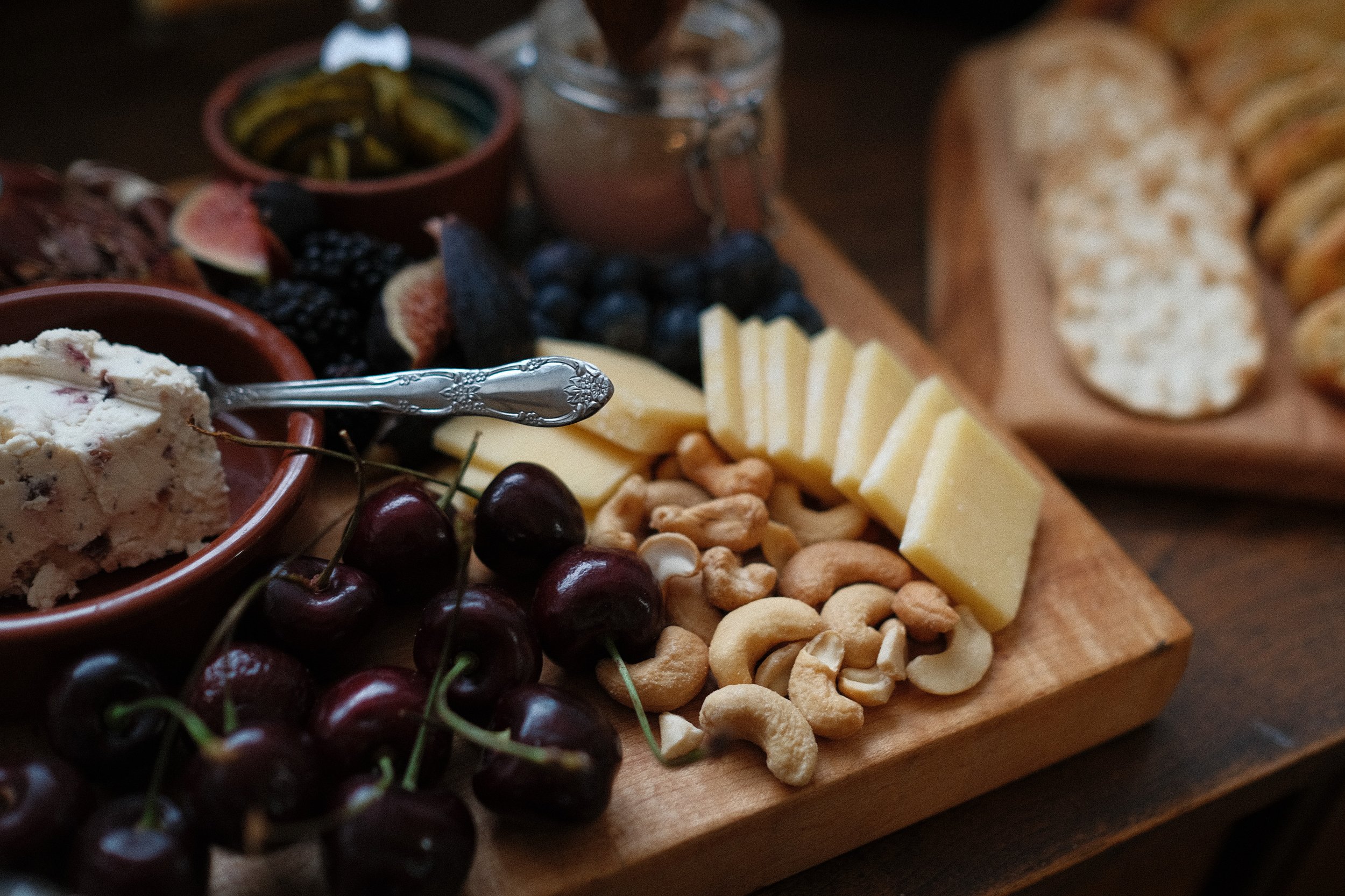 An assortment of cheese, fresh cherries, cashews, blueberries, figs, and sliced bread on a wooden serving tray.