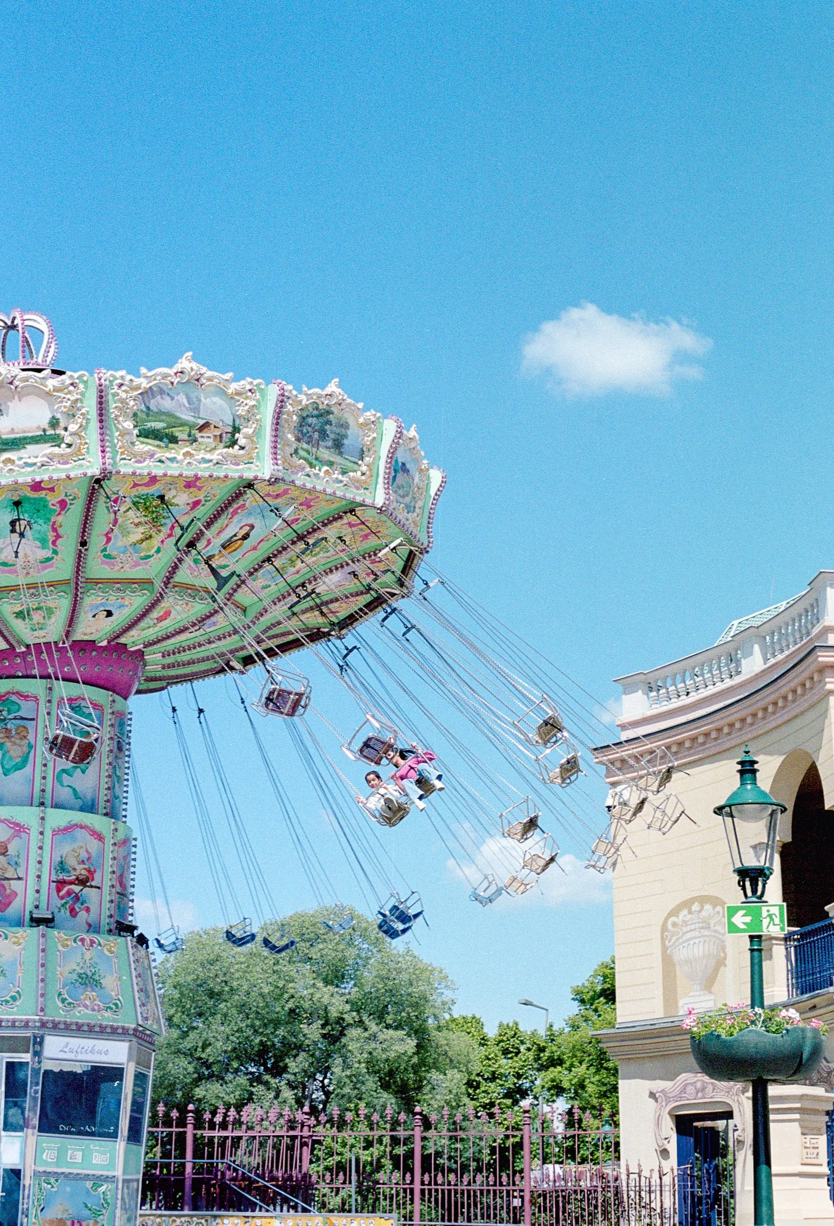 A carousel ride at an amusement park with children on the swings, under a blue sky with a few clouds.