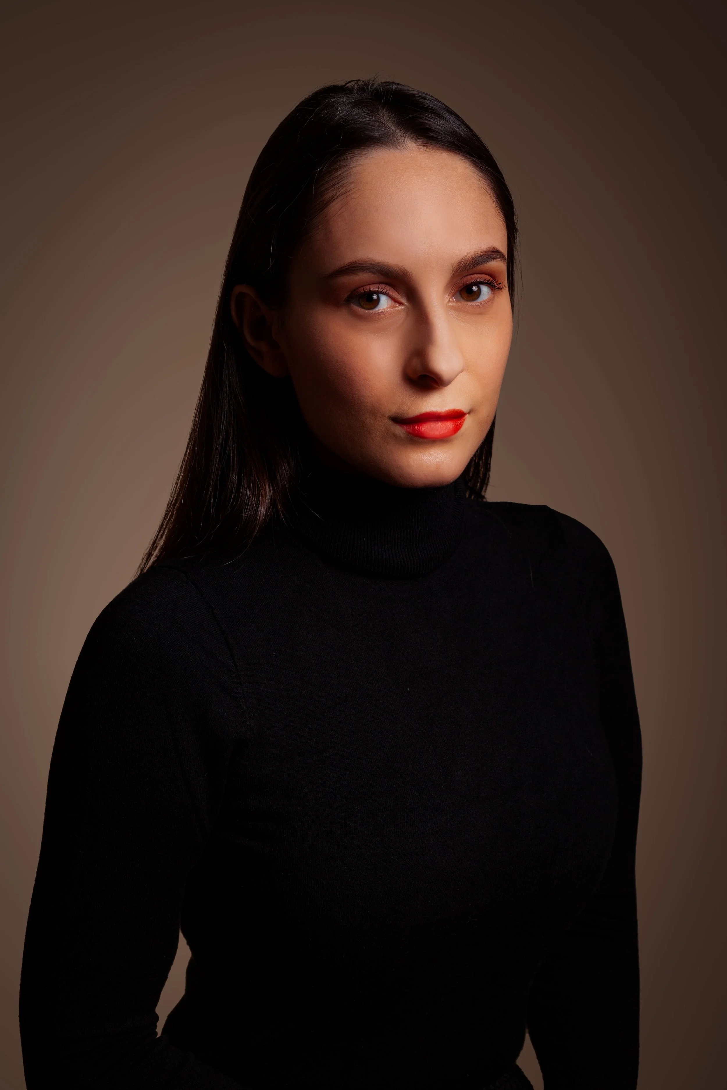 A portrait of a woman with long dark hair wearing a black turtleneck, looking at the camera with a neutral expression against a plain background.