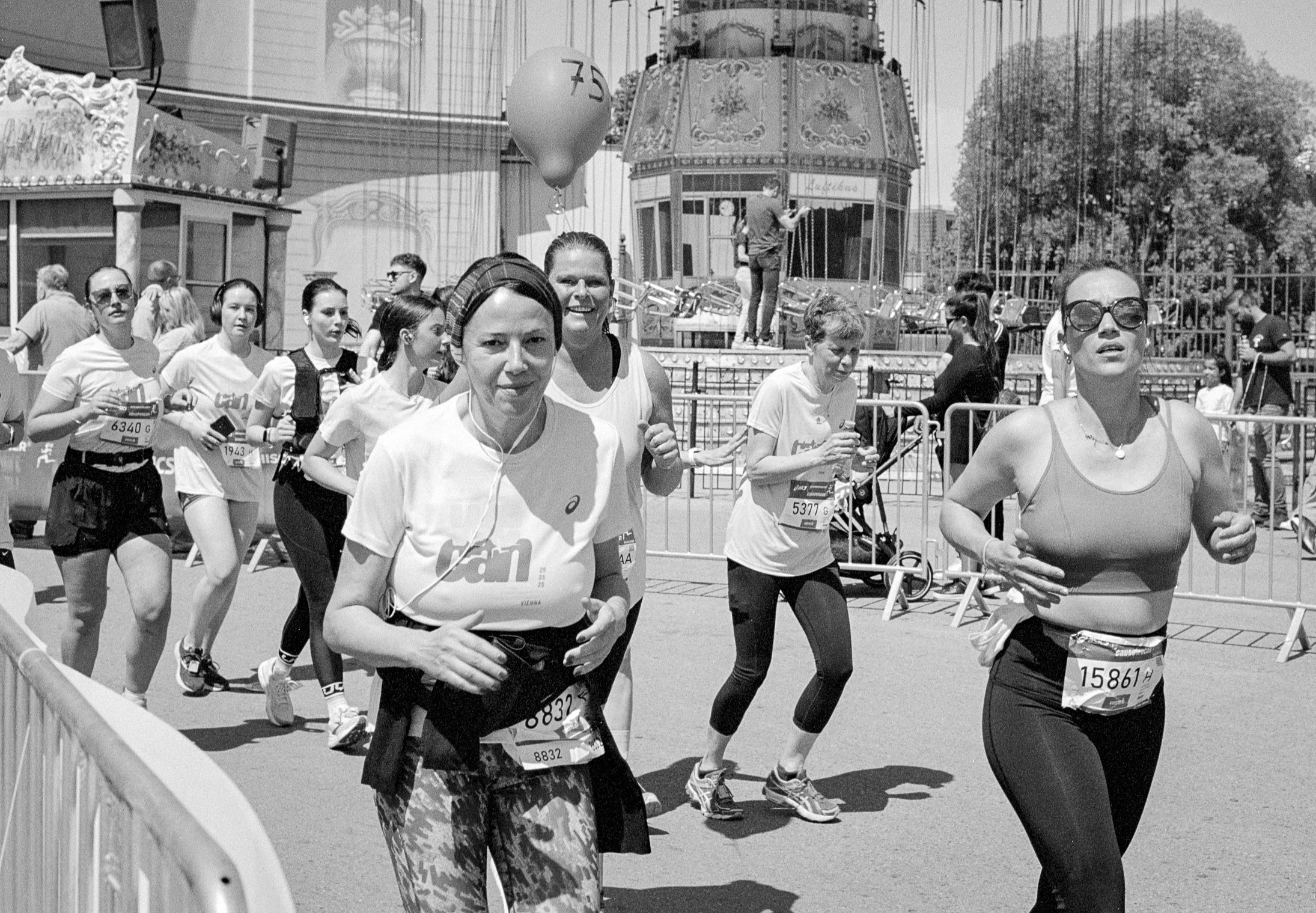 People participating in a marathon race, running outdoors near a carnival ride with a backdrop of trees.