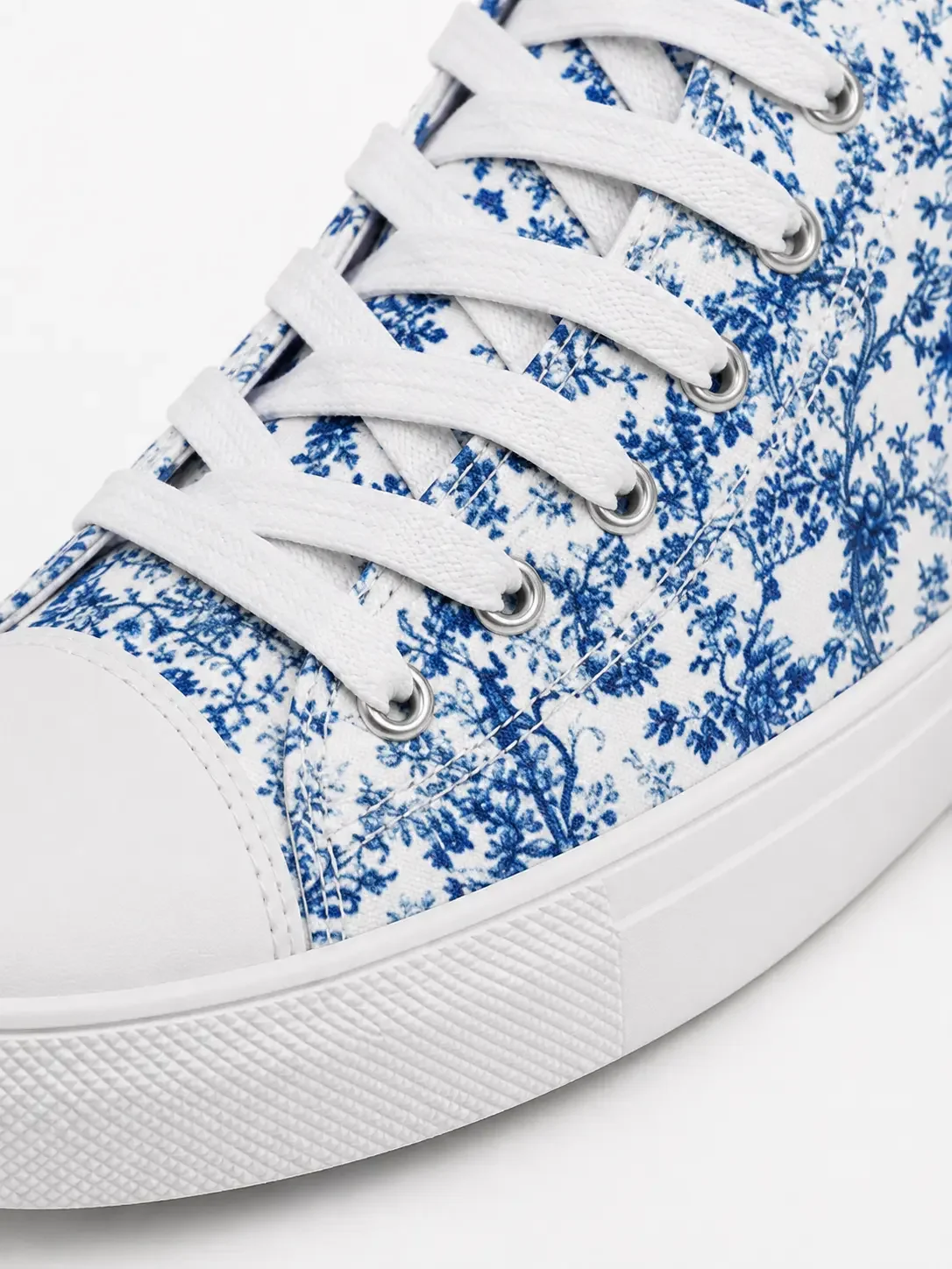 Close-up of a white canvas high-top sneaker featuring an intricate blue floral toile pattern and white laces.