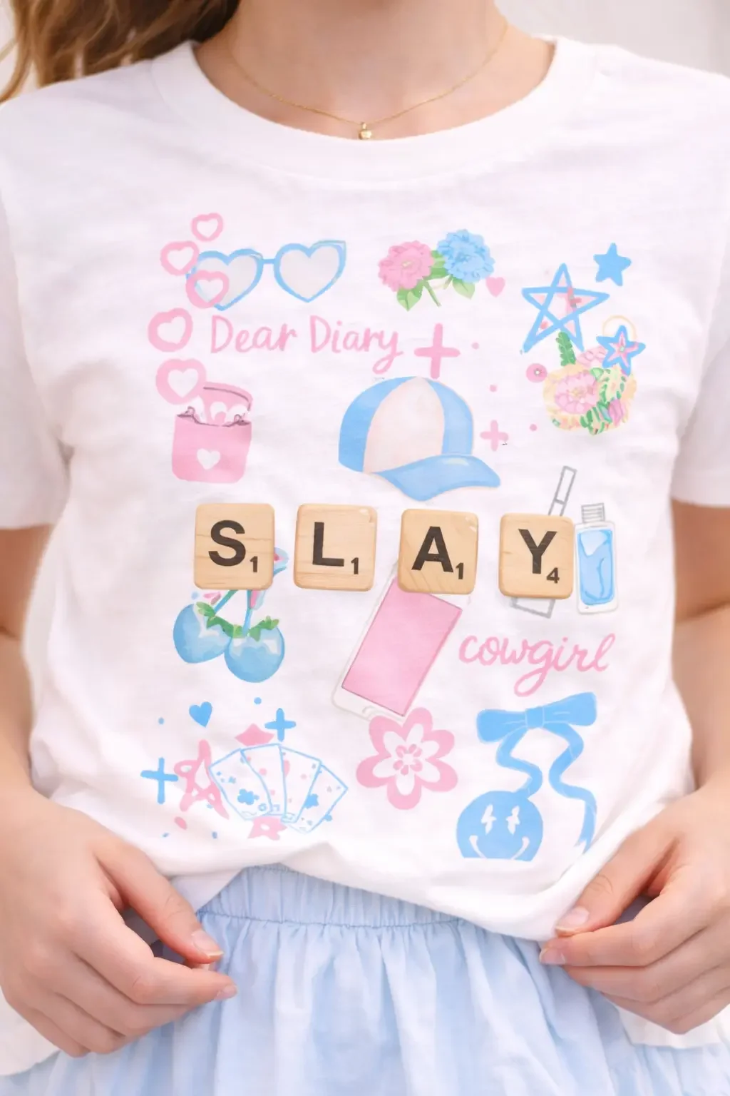Close-up of a girls white graphic tee showing a "SLAY" doodle icon graphic design.