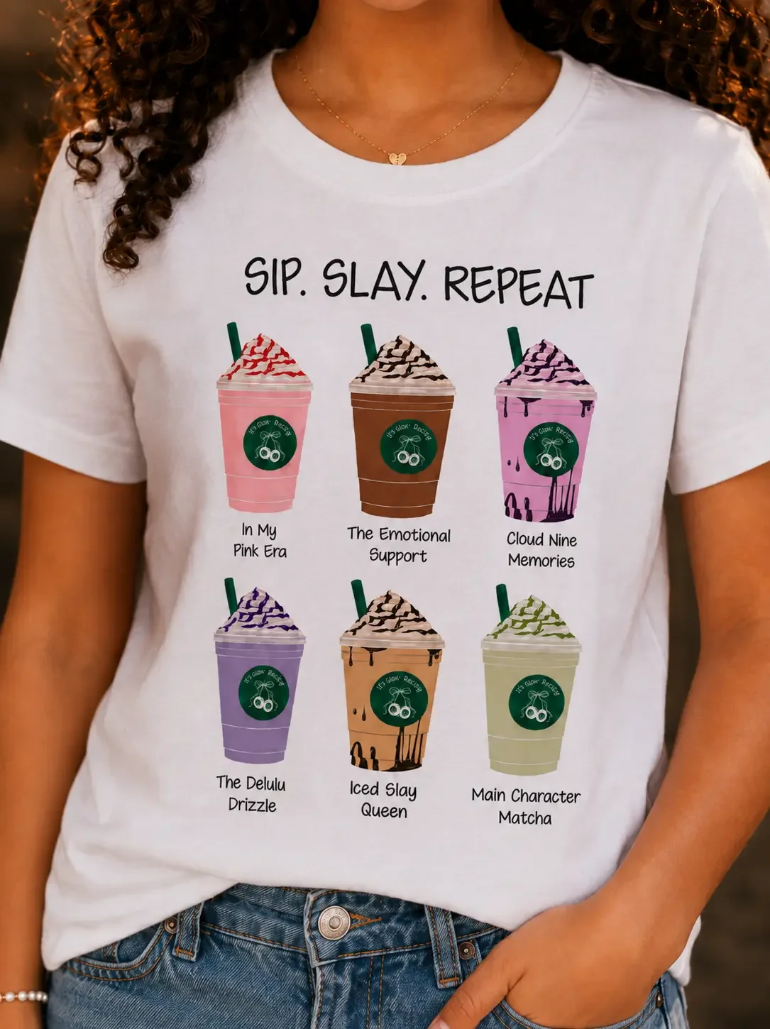 Close-up of a white graphic t-shirt with Sip Slay Repeat text above six cartoon iced coffee illustrations.