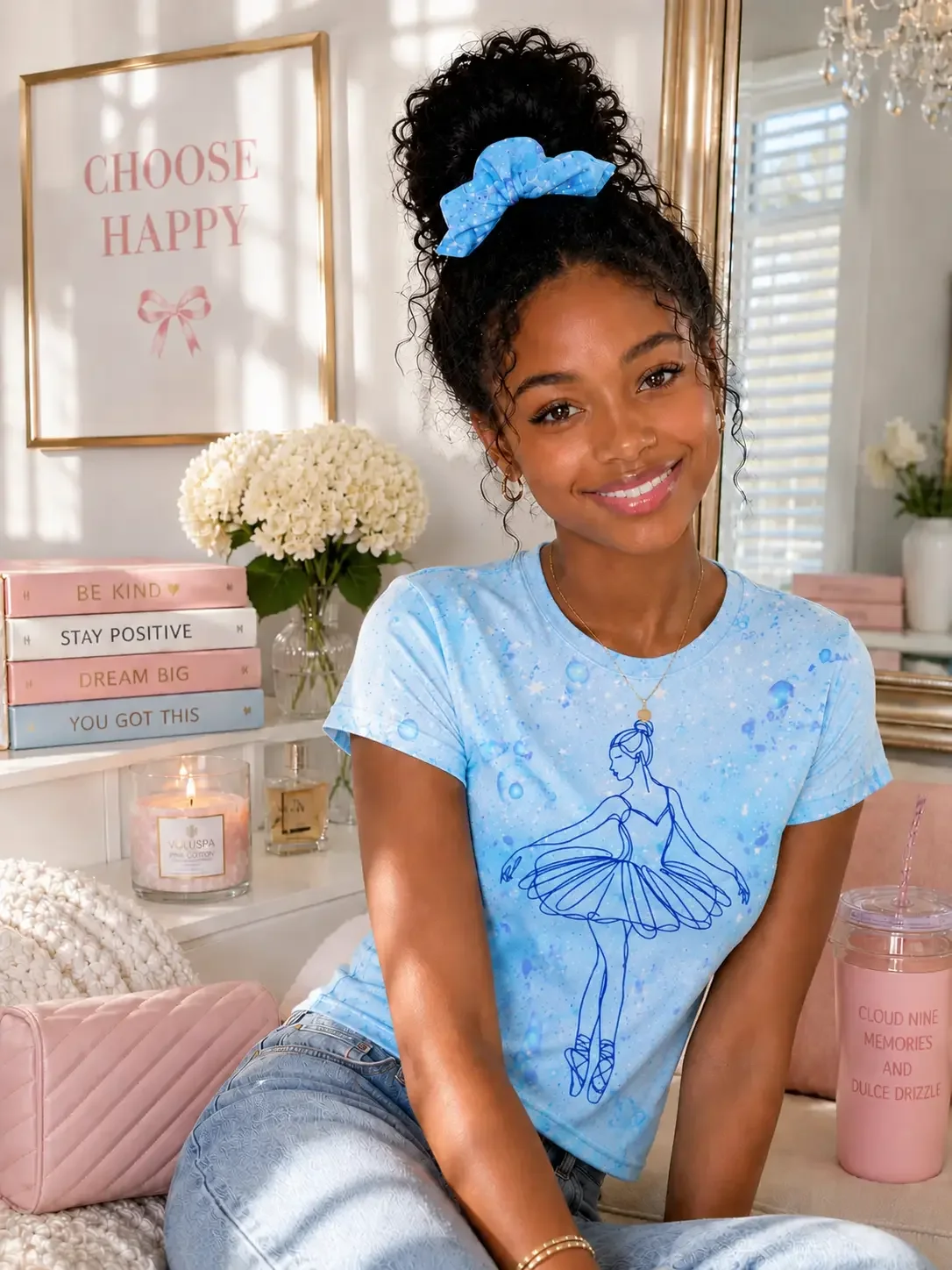 Smiling woman with dark curly hair in a bun wearing a blue star bow scrunchie, matching graphic t-shirt, and light wash jeans.