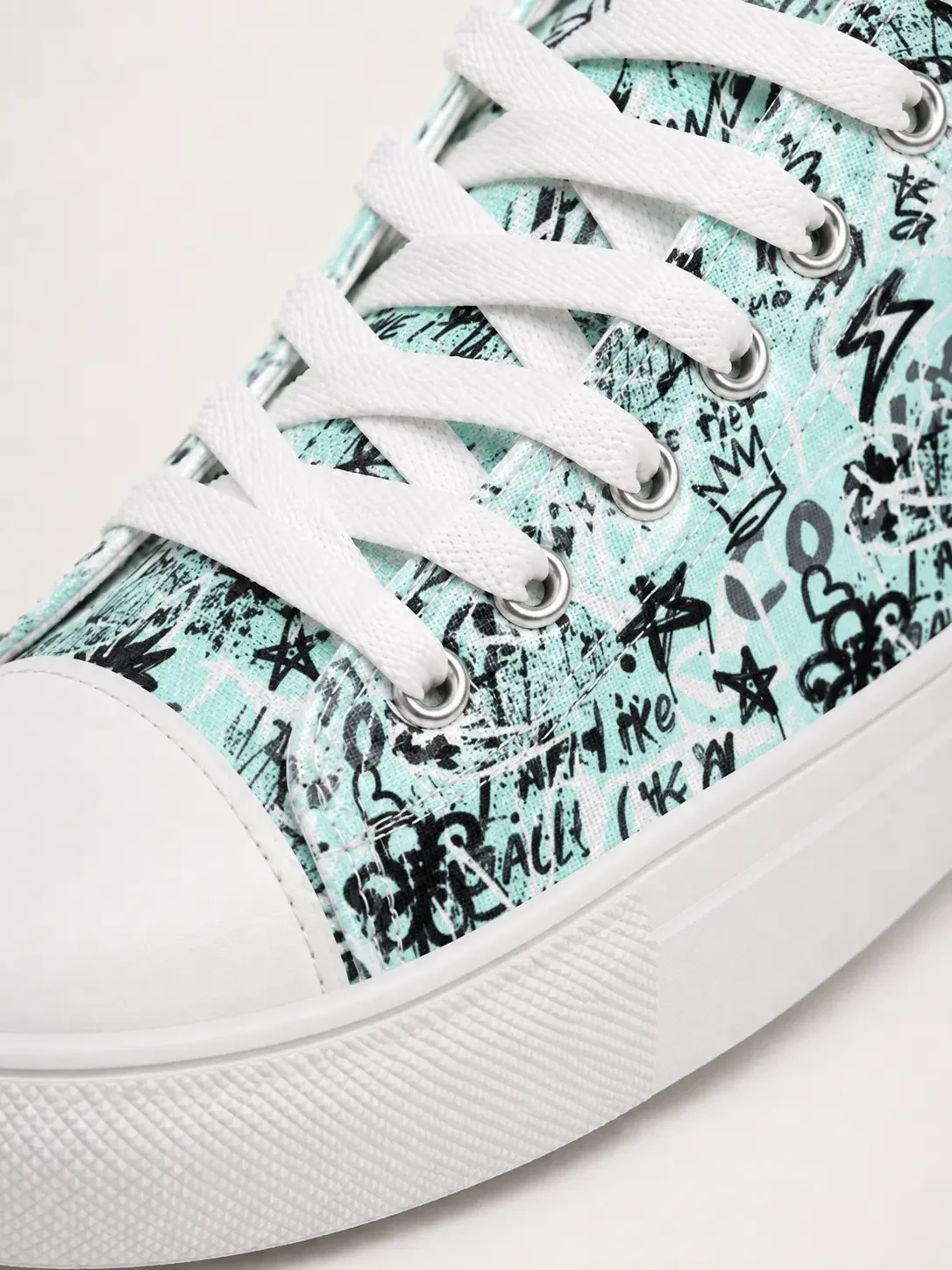 Close-up of a mint green canvas high-top sneaker featuring an edgy black graffiti doodle print pattern and white laces.