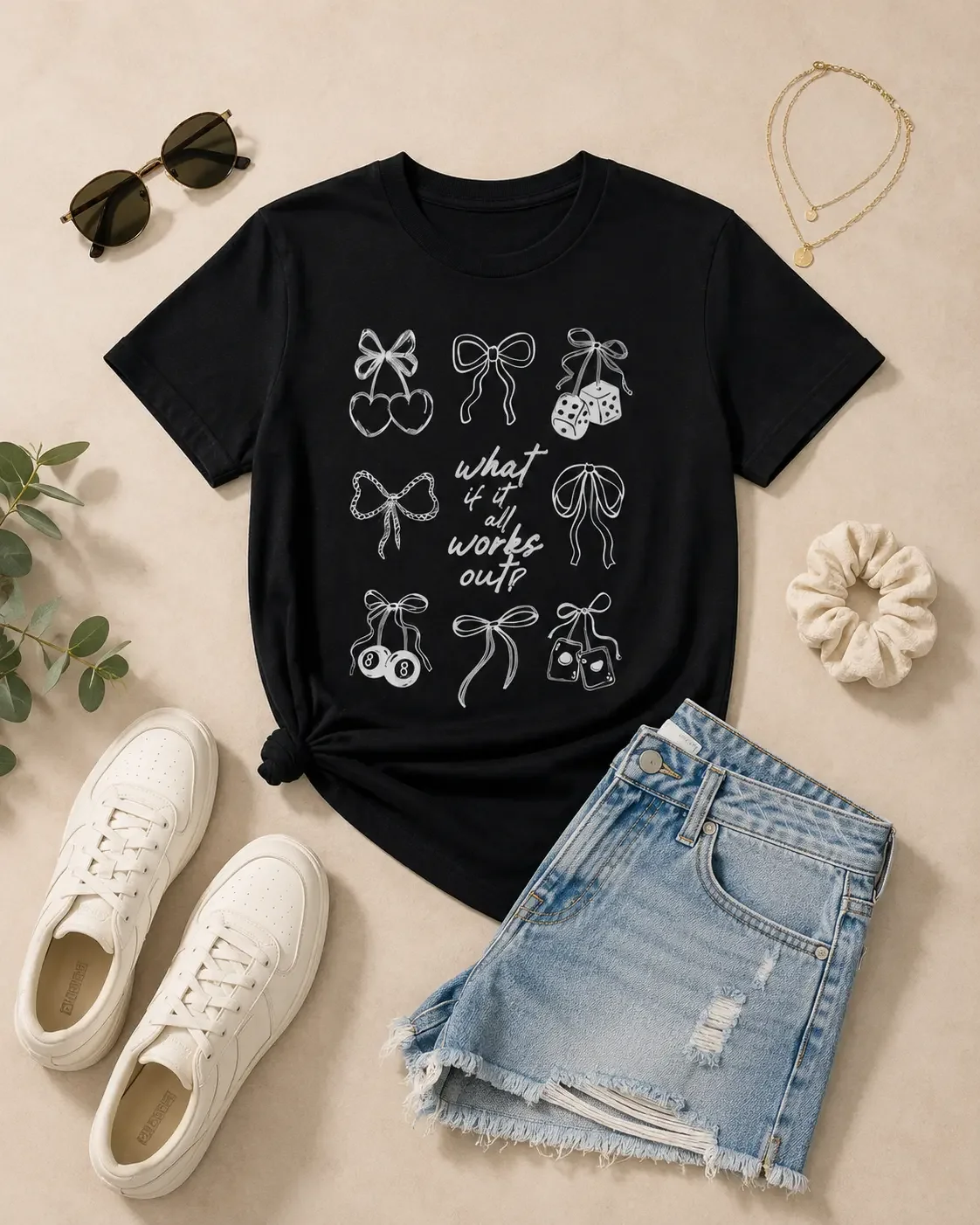 Flat lay display of a black what if it all works out graphic tee, denim shorts, white sneakers, and accessories.