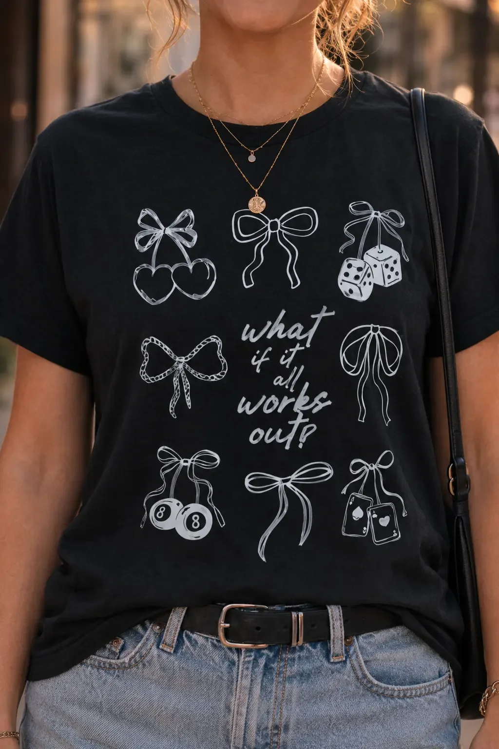 Close-up view of a black crew neck t-shirt featuring a handwritten quote surrounded by white ribbon bow graphics.