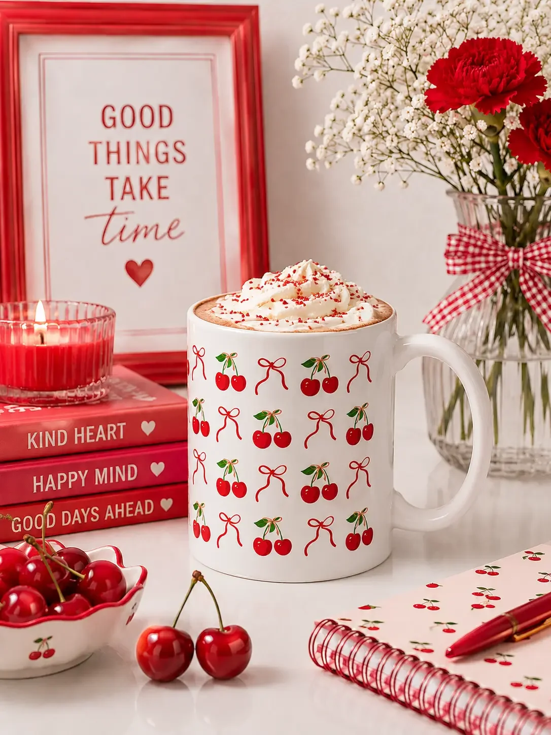 White mug with cherries and bows pattern filled with whipped cream on a desk with red books and fresh cherries.