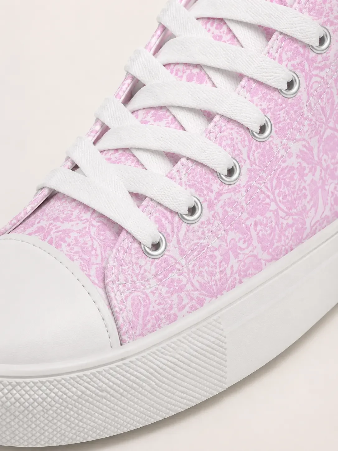 Close-up detail of white canvas shoelaces, eyelets, and a rubber sole with a pink toile print pattern design.