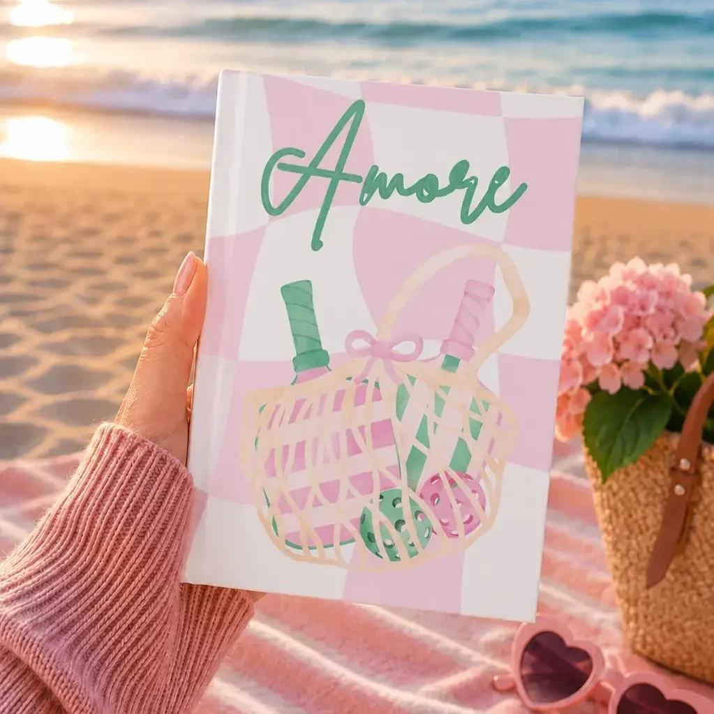 beach-hand-holding-pink-amore-pickleball-journal.webp