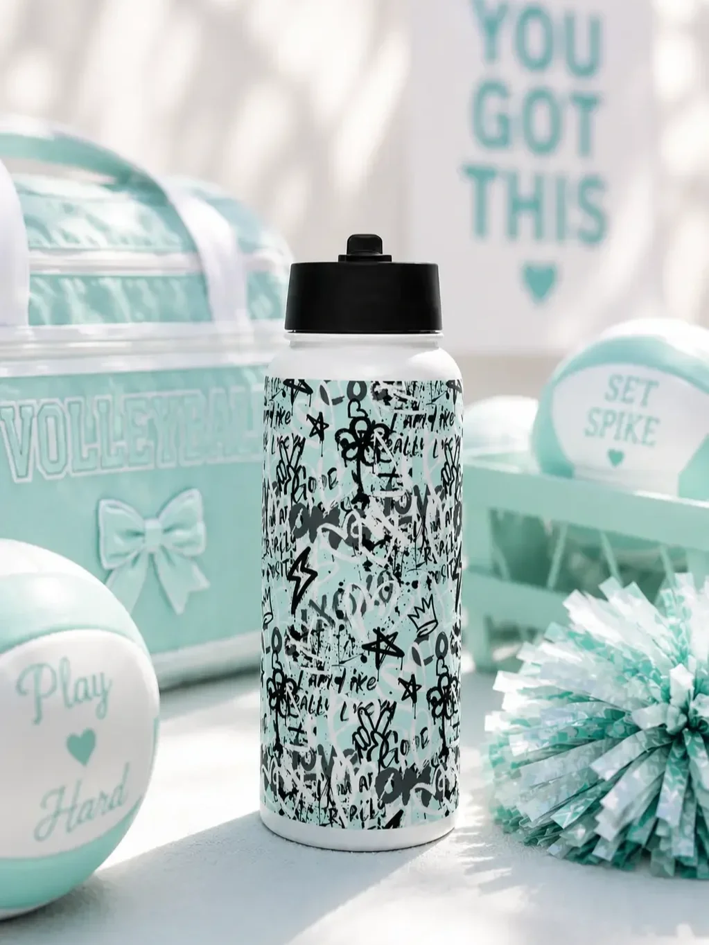A graffiti water bottle sits by a mint volleyball bag, pastel volleyballs, a pom-pom, and a sign reading "YOU GOT THIS".