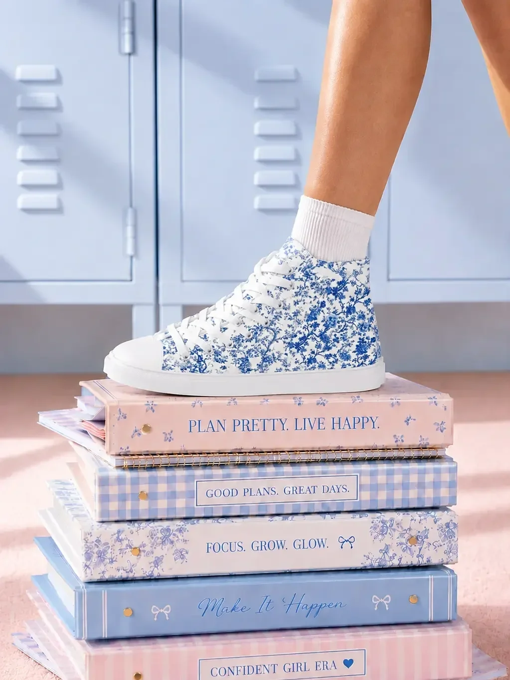 A person wearing a blue floral toile print high-top canvas sneaker stepping on a stack of pastel aesthetic binders.