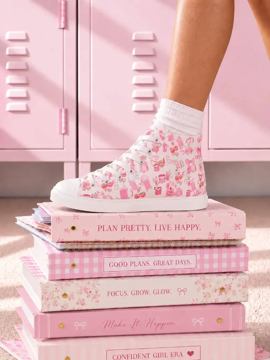 A person wearing white canvas high-top sneakers with a pink doodle pattern standing on pink preppy journals by school lockers.