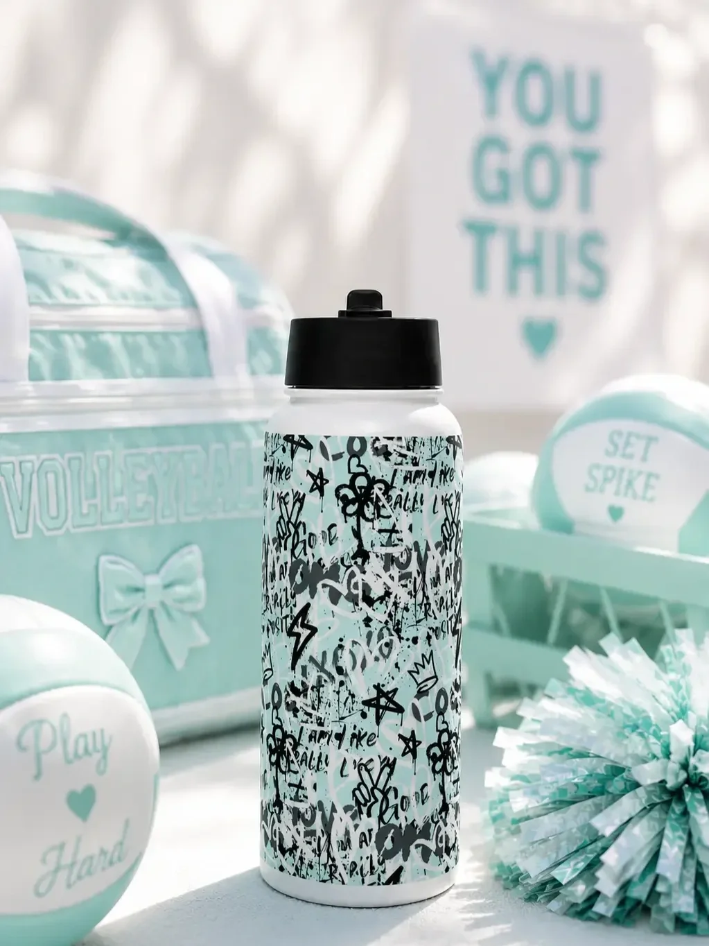 A graffiti water bottle sits by a mint volleyball bag, pastel volleyballs, a pom-pom, and a sign reading "YOU GOT THIS".