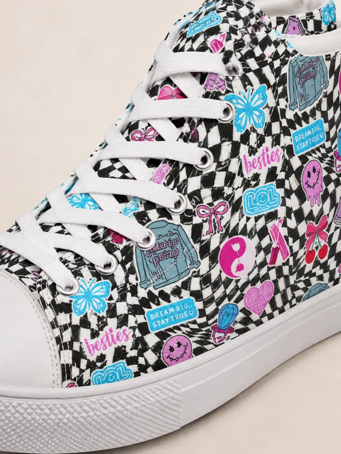 Close-up detail of white canvas laces, rubber sole, and a black and white checkered canvas material with colorful sticker doodles.