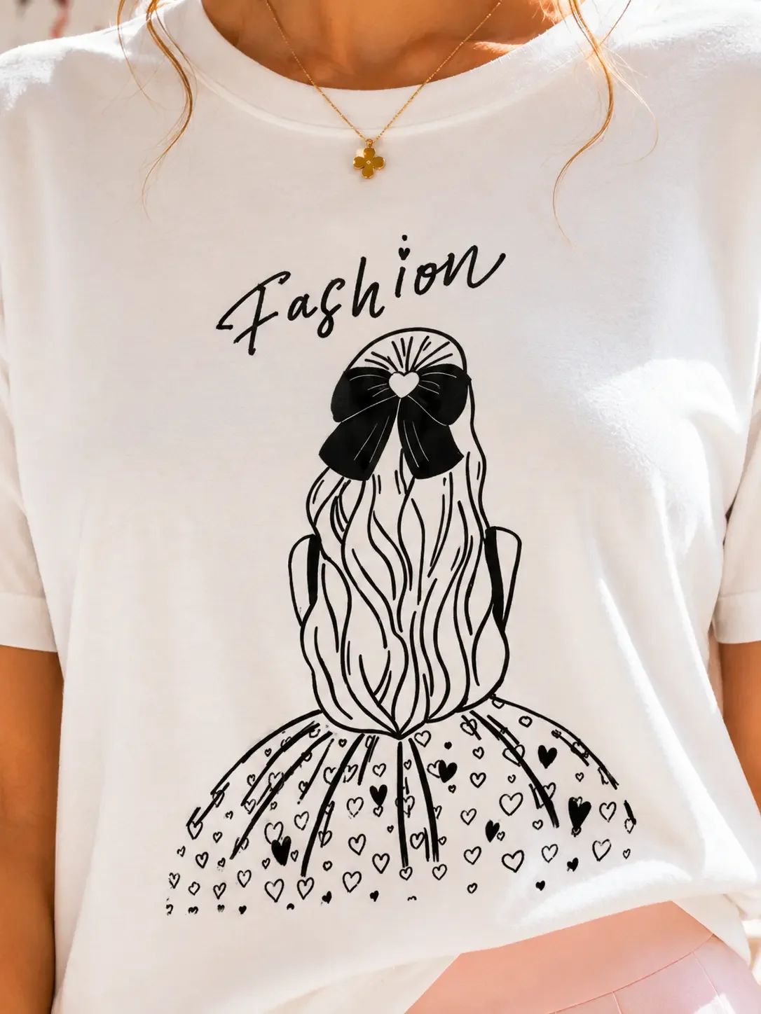 Close-up of a white graphic t-shirt featuring a black line art design of a girl with a bow and the word Fashion.