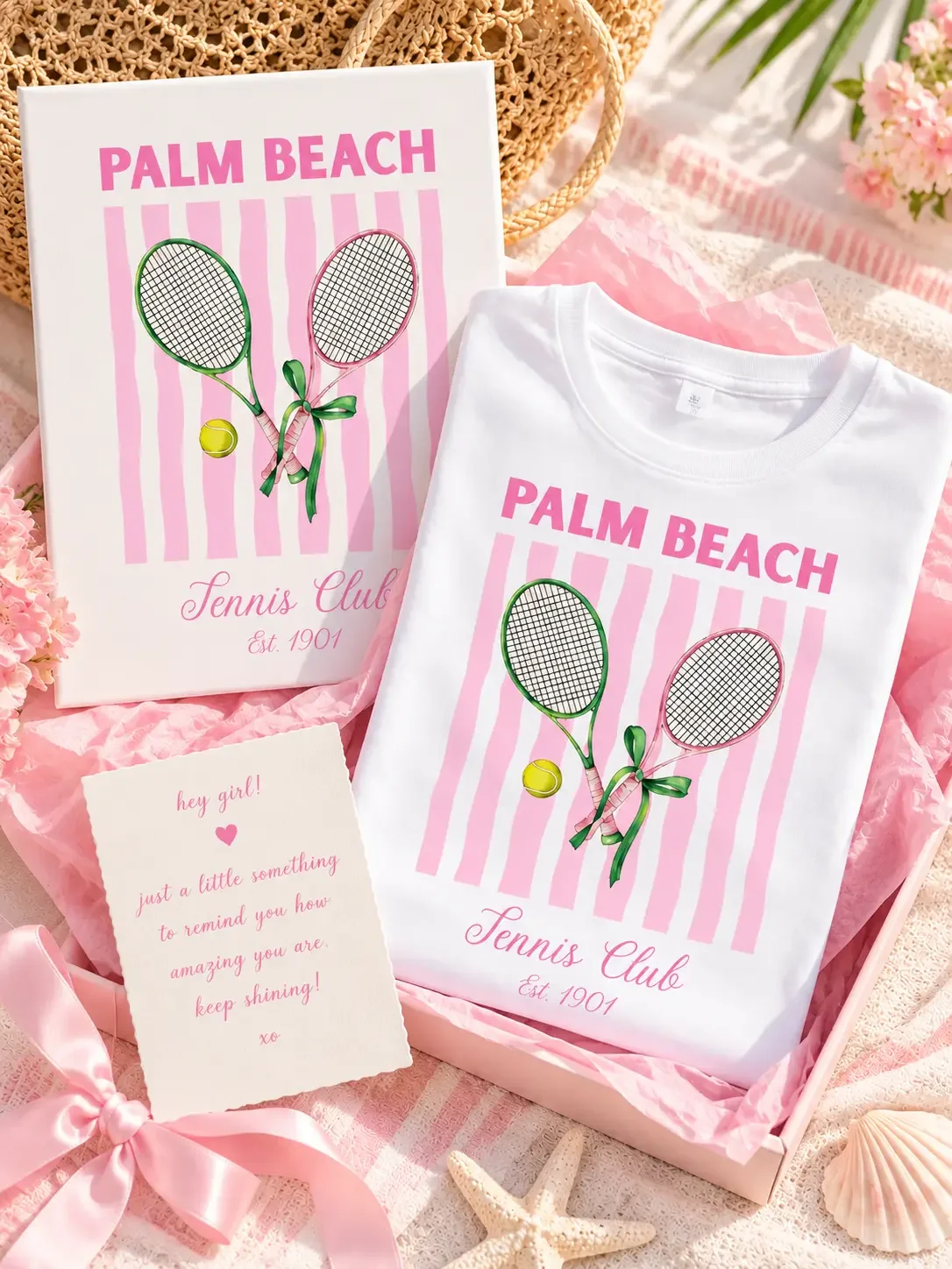 Open pink gift box containing a folded white Palm Beach Tennis Club t-shirt, matching wall art canvas, and a pink motivational note card.