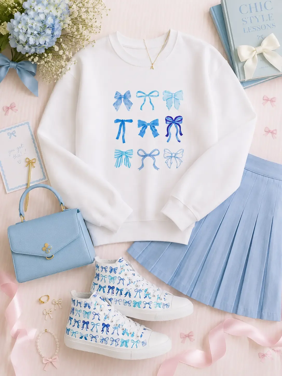 Product view of a white crewneck sweatshirt laid flat showcasing a 3x3 grid design of various light and royal blue watercolor ribbon bows.