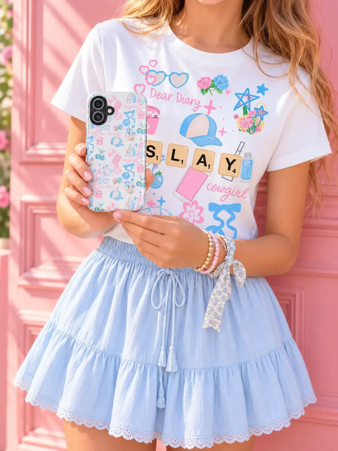 Close-up of a girl wearing a "Slay Cowgirl" graphic tee and a blue ruffle skirt while holding a matching phone case.