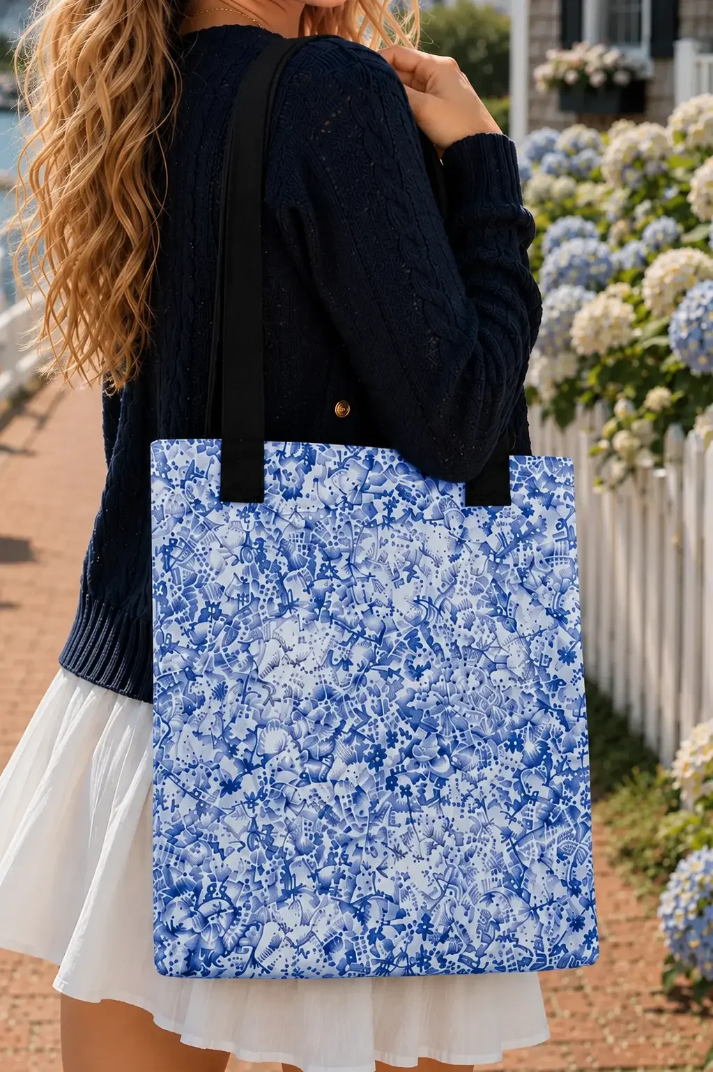 White canvas tote bag with an all-over intricate blue floral porcelain-style pattern carried over a model's shoulder.